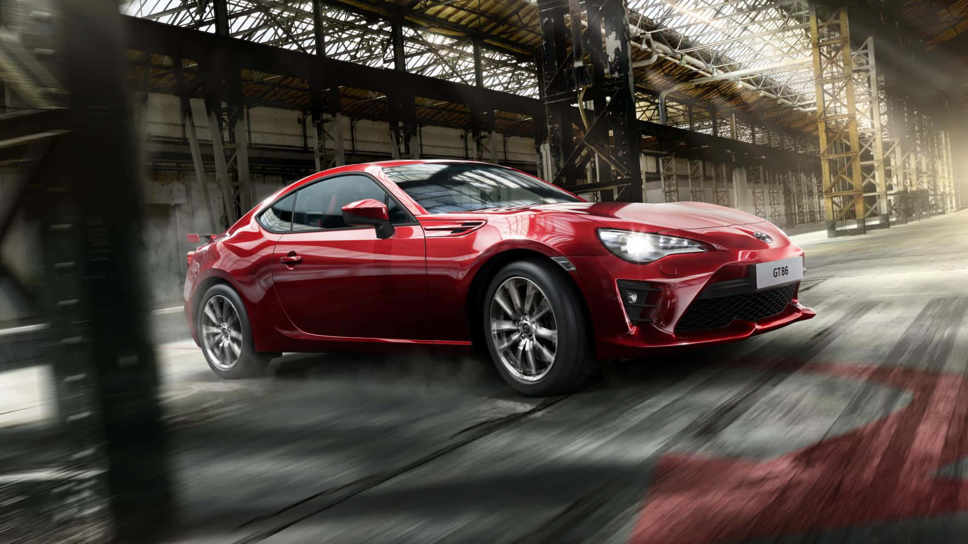 4K 紅色 Toyota 86 車輛高速駕駛 壁紙 — 一輛充滿活力的紅色跑車在廢棄的工業倉庫中疾馳，帶有動態模糊和戲劇性燈光。
