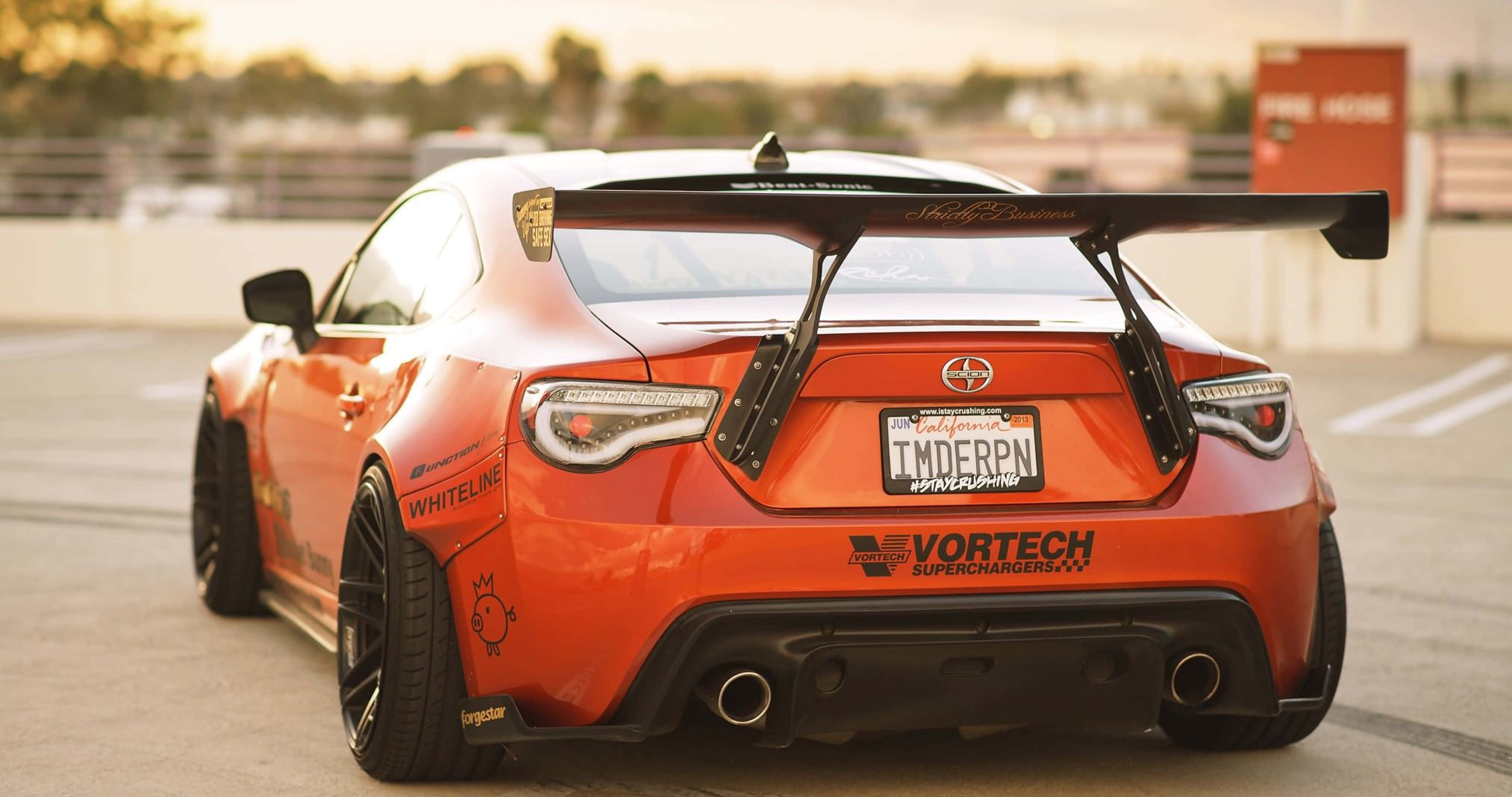 以創新科技駕馭自信，4K Toyota 86帶來極致駕馭體驗 壁紙 — 一架充滿活力的橙色改裝跑車，帶有大型後翼，停泊在陽光普照的停車場。