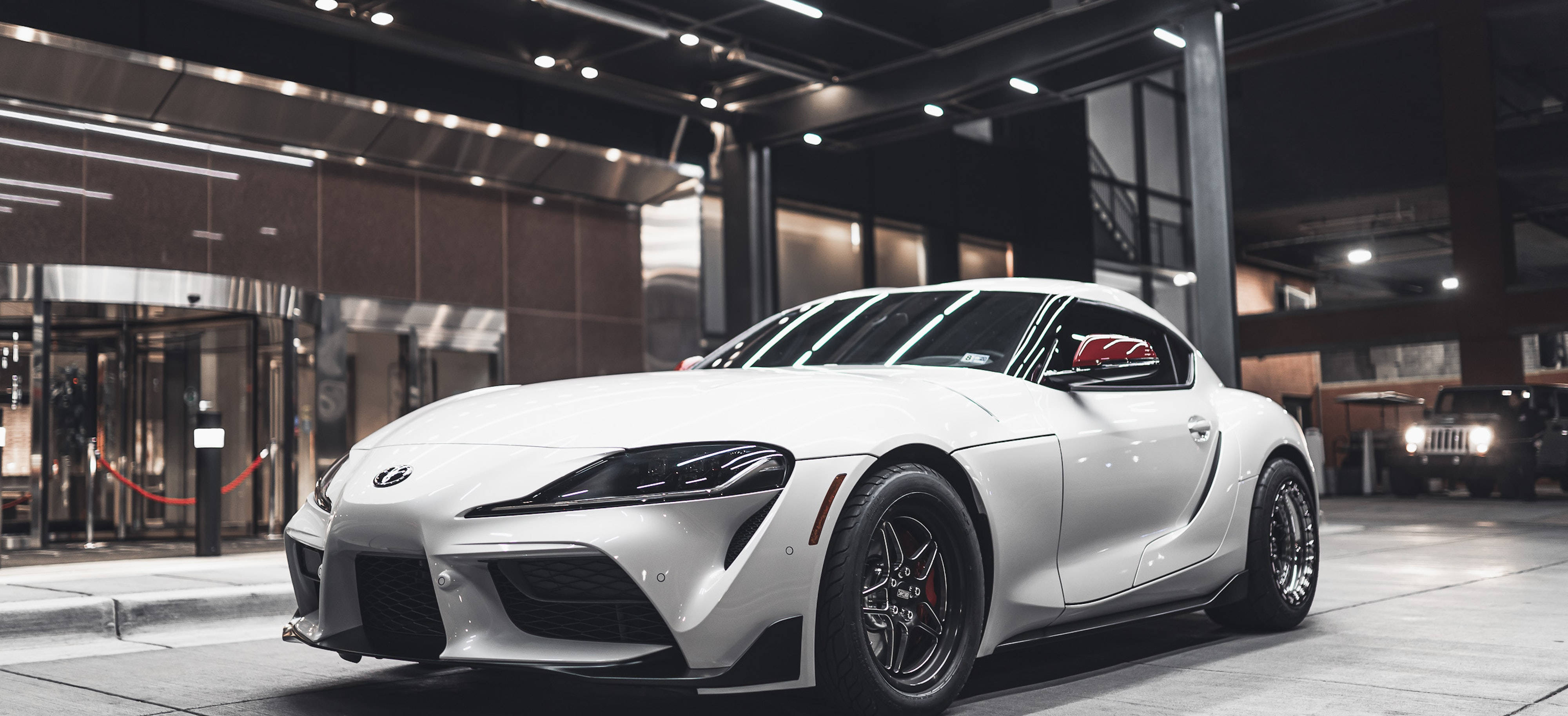 4K 《Toyota Supra》白色車款展示 壁紙 — 一輛時尚的白色跑車配黑色輪圈，停放在現代城市車庫的明亮燈光下。