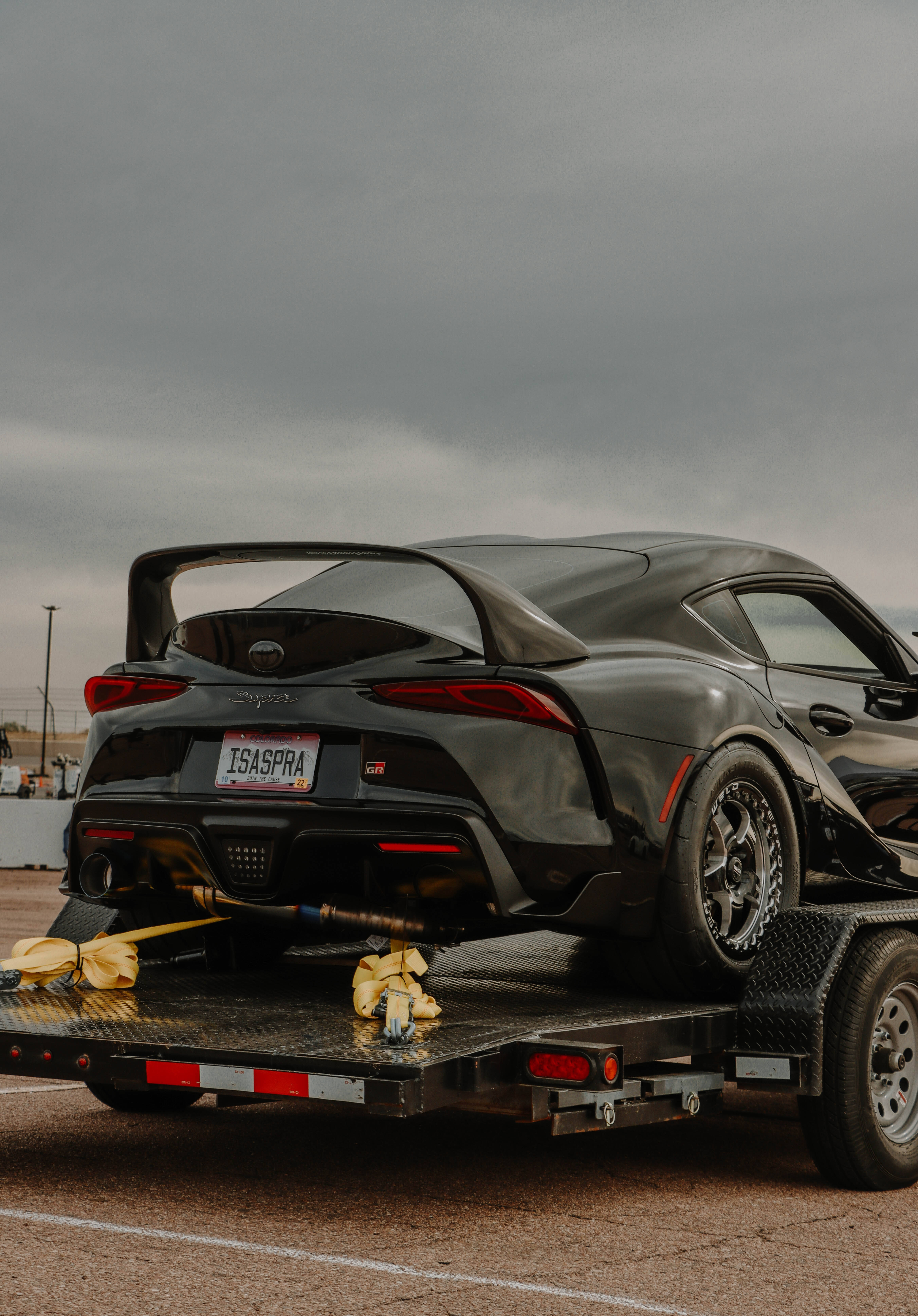 4K 《Toyota Supra》黑色車款於運輸卡車上 壁紙 — 一架型格黑色豐田GR Supra跑車停泊在平板拖車上，天空多雲。