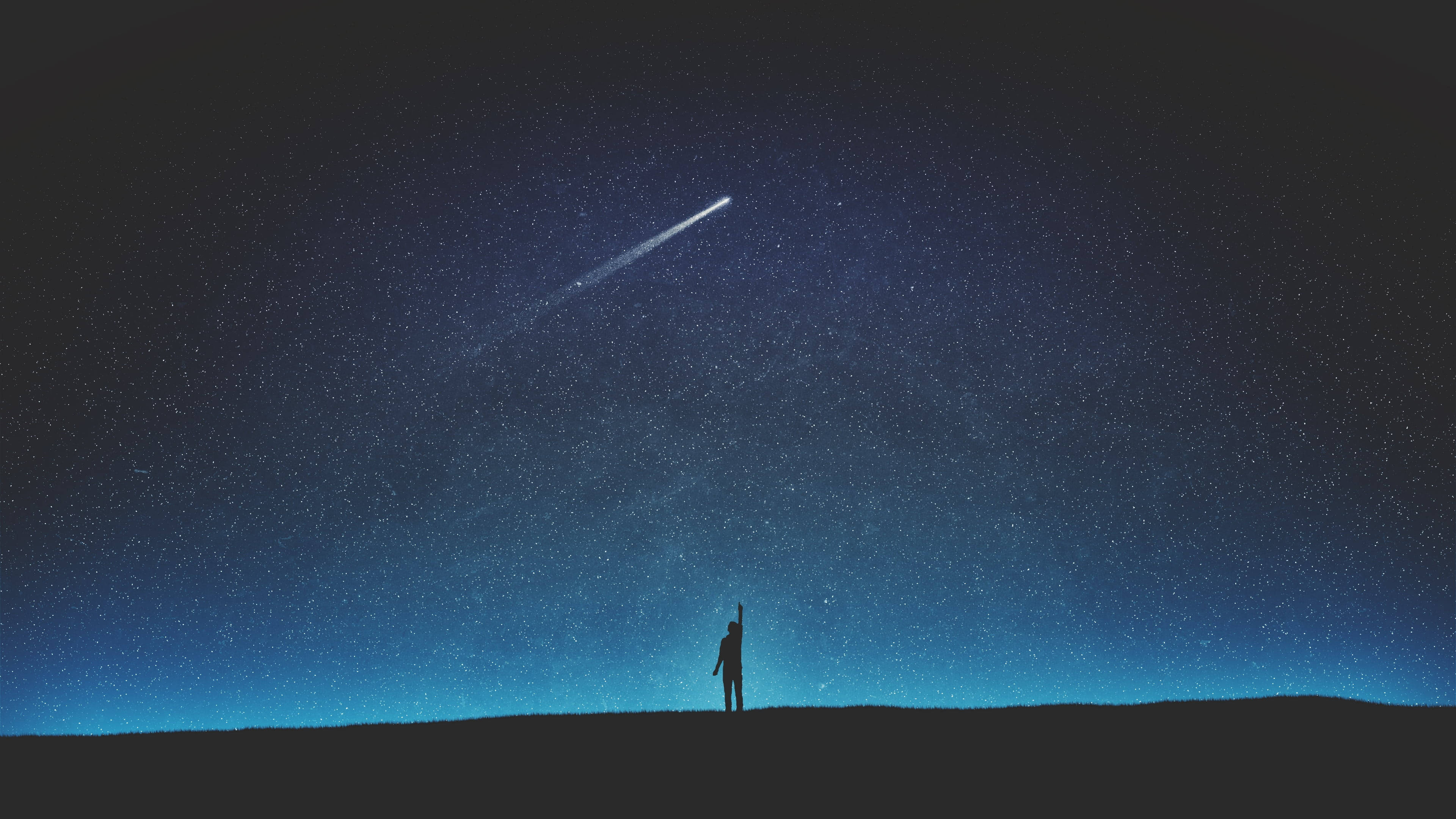月光下的剪影 4K 天空 壁紙 — 一個孤獨的身影在夜晚站在山丘上，伸手朝向一顆明亮的流星劃過滿天繁星的靛藍色天空。