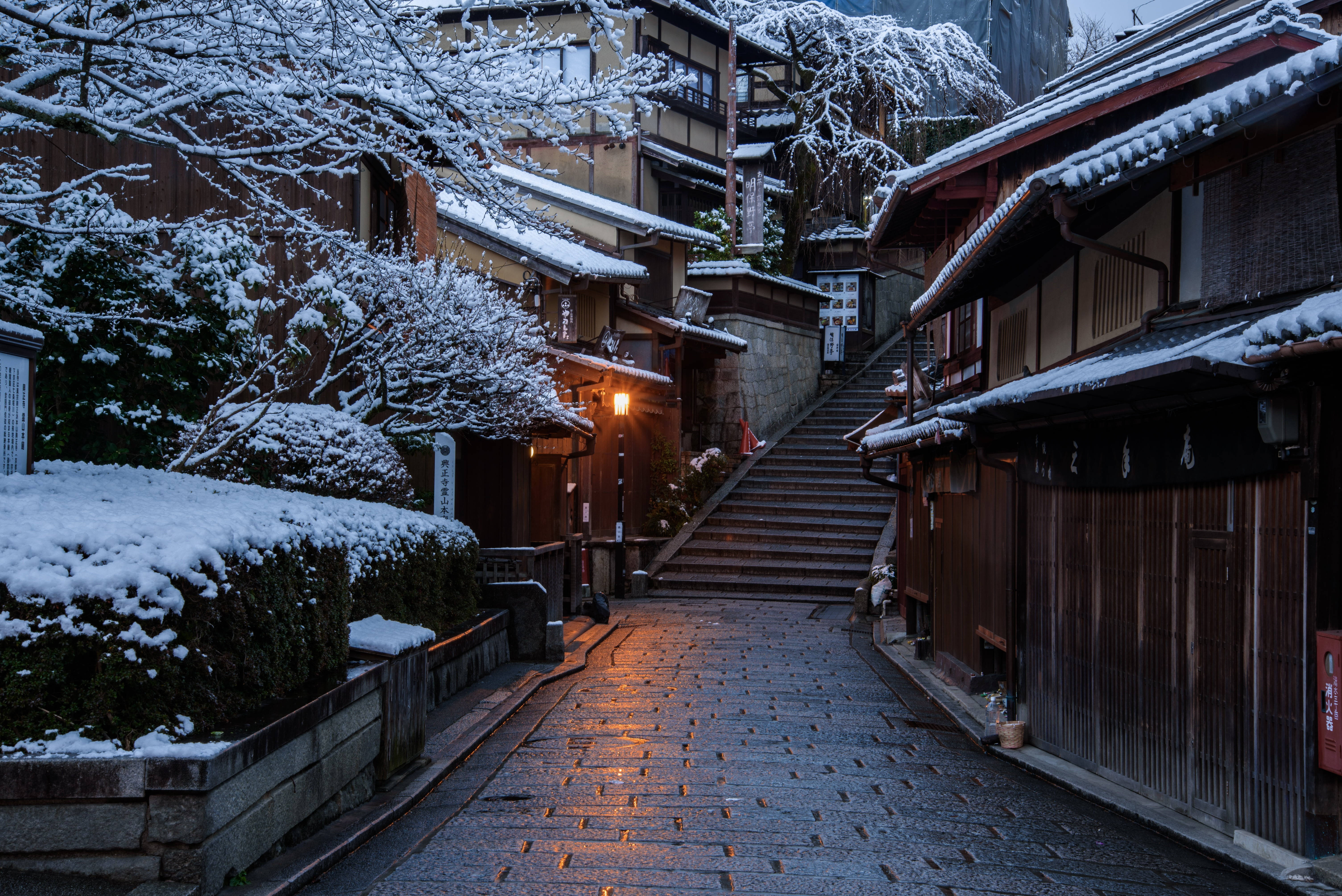 雪中京都日本4K 壁紙 — 一條灑滿雪嘅傳統日本街道，夜晚溫暖嘅燈籠光線喺濕滑嘅石階上反射。