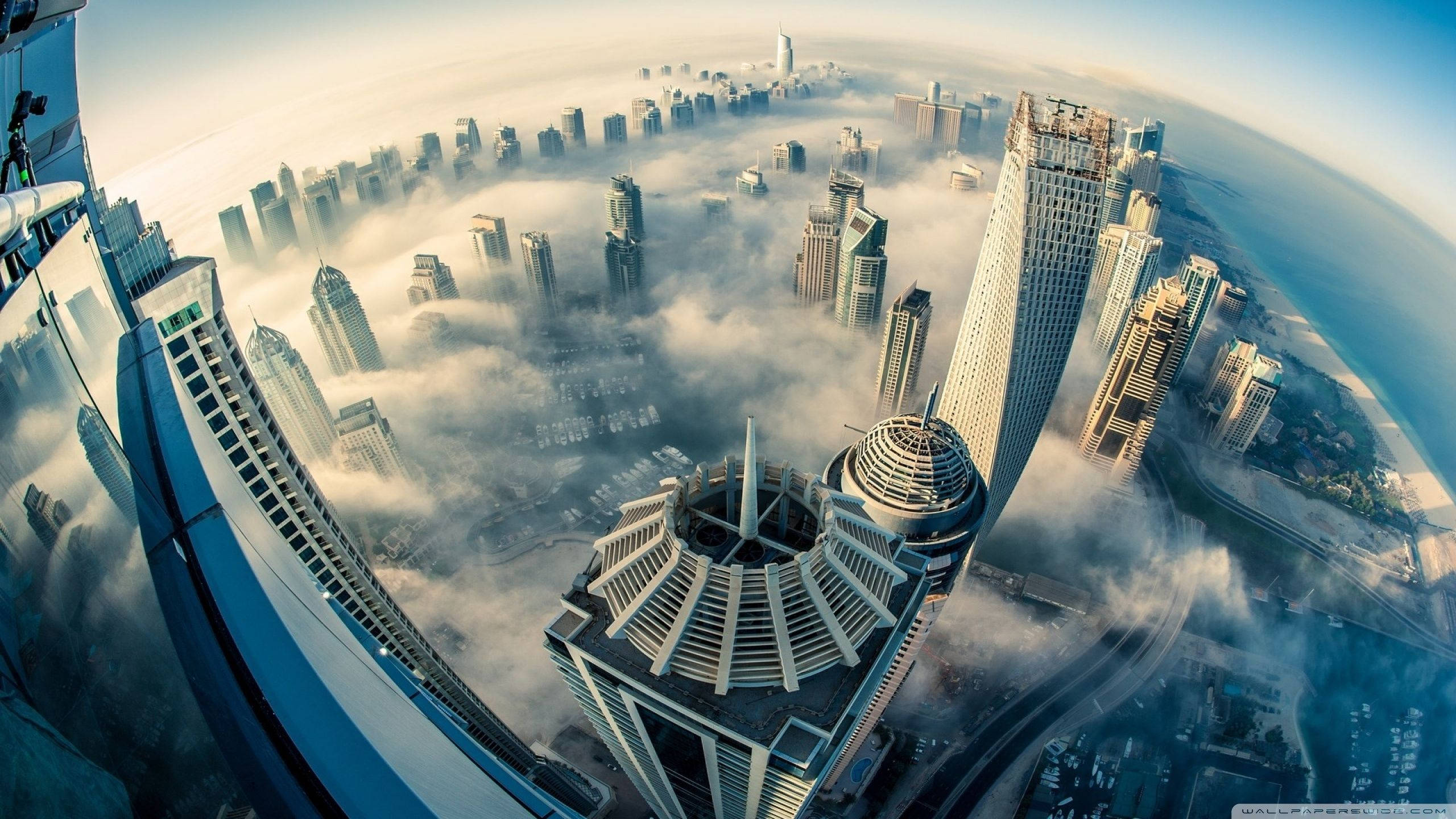 4K高畫質現代摩天大樓城市景觀 壁紙 — 魚眼視角下的未來城市景觀，高聳的摩天大樓從雲層中浮現，沐浴在金色的日出光芒中。