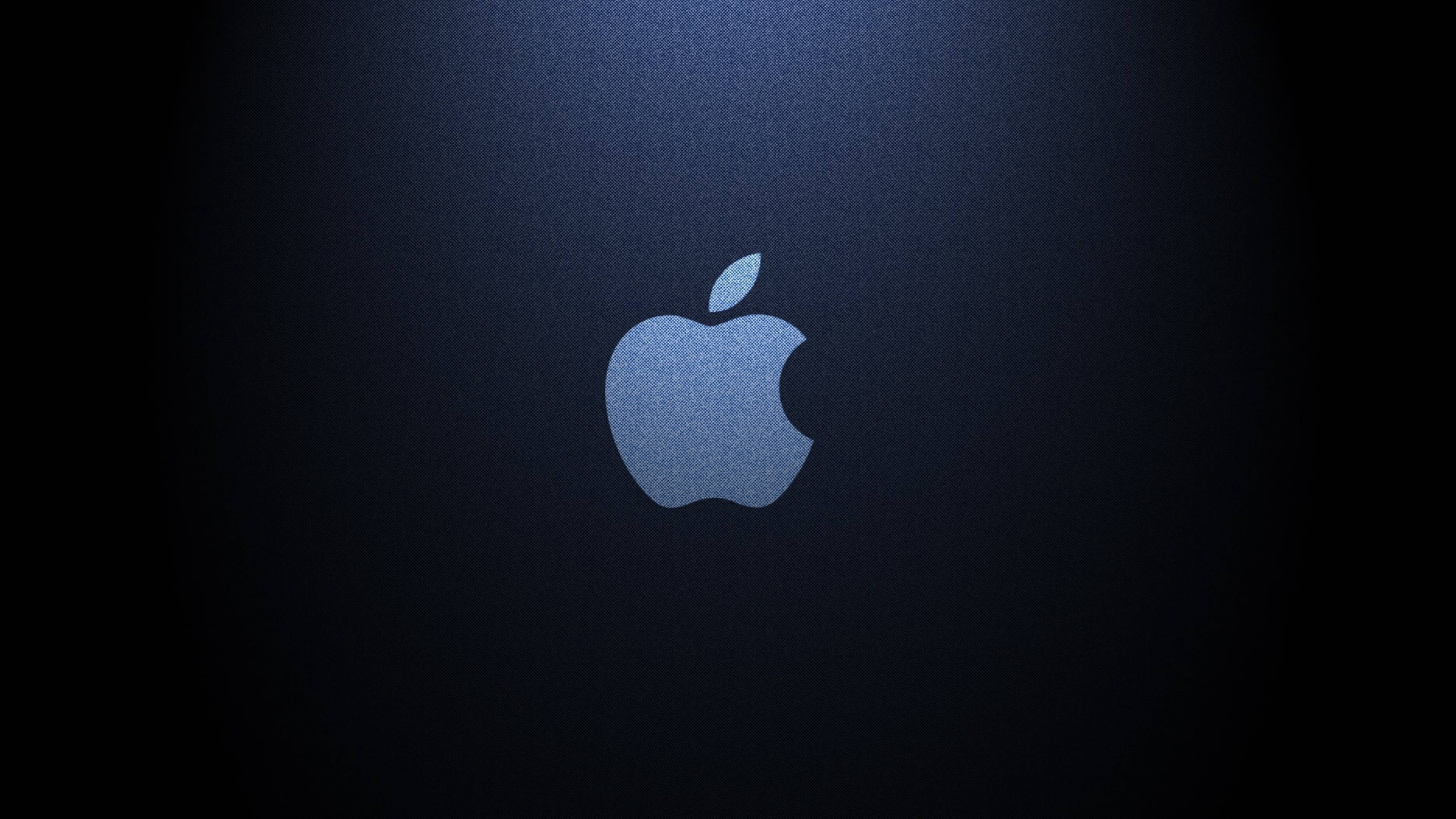深藍牛仔蘋果4K超高清 壁紙 — 發光的Apple標誌居中在深藍色紋理背景上，帶有聚光燈效果。