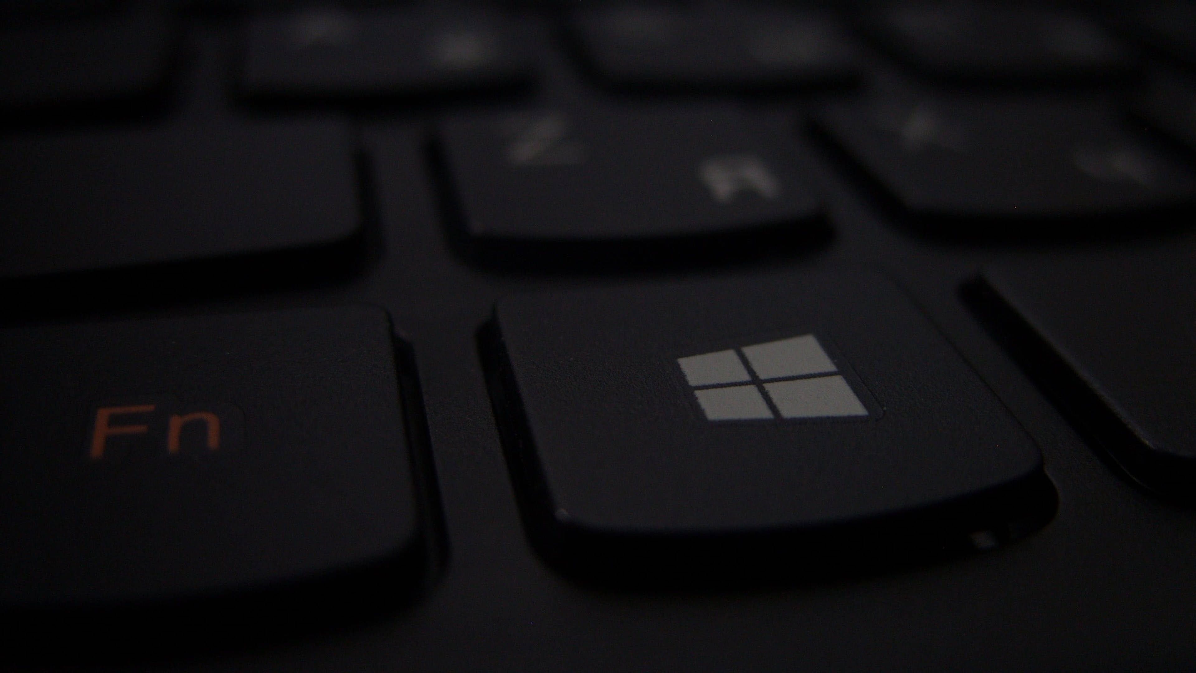 4K 筆記型電腦 Windows 鍵特寫 壁紙 — 暗色鍵盤嘅特寫，喺低光環境下帶有發光橙色 Fn 鍵同亮起嘅 Windows 標誌鍵。