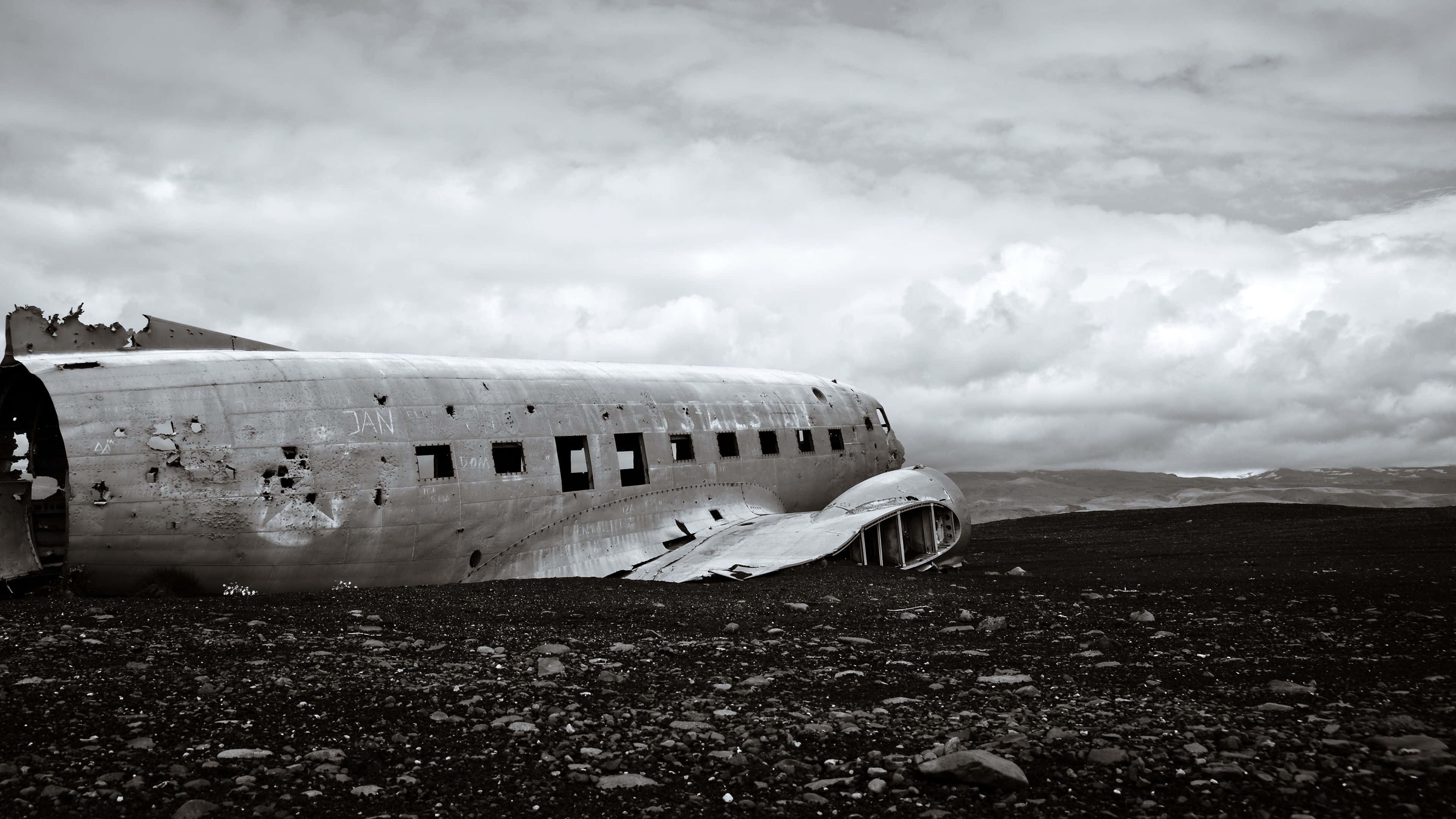 4K 飛機墜毀黑白畫面 壁紙 — 一架風化的飛機機身被遺棄在陰天下荒蕪的岩石平原上。