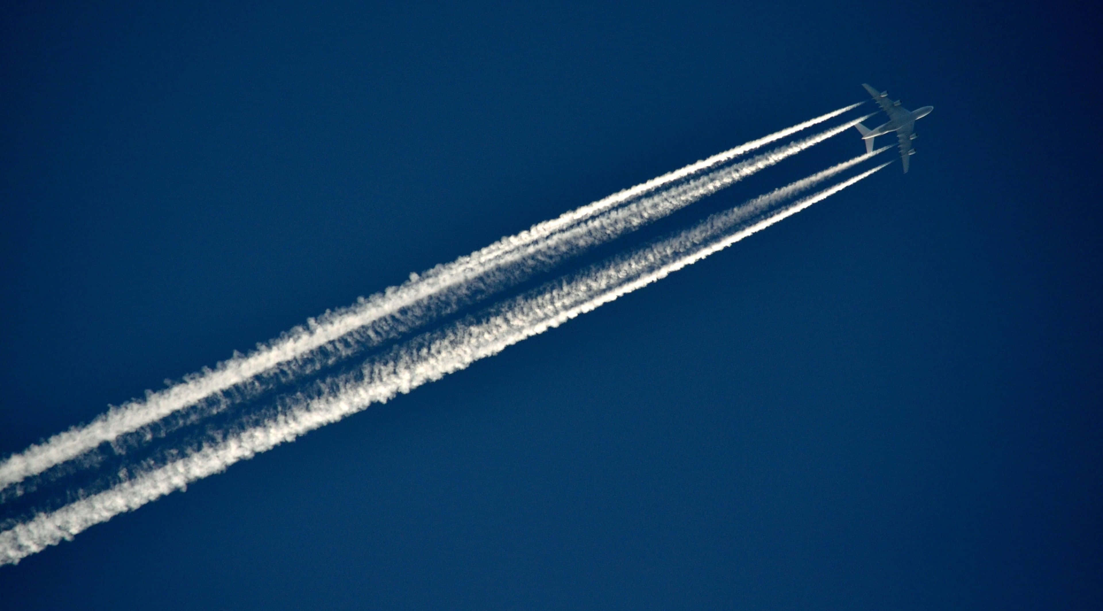 虛擬飛行：體驗4K飛機 壁紙 — 一架商用飛機在深藍色天空中留下三條明顯的白色凝結尾跡。