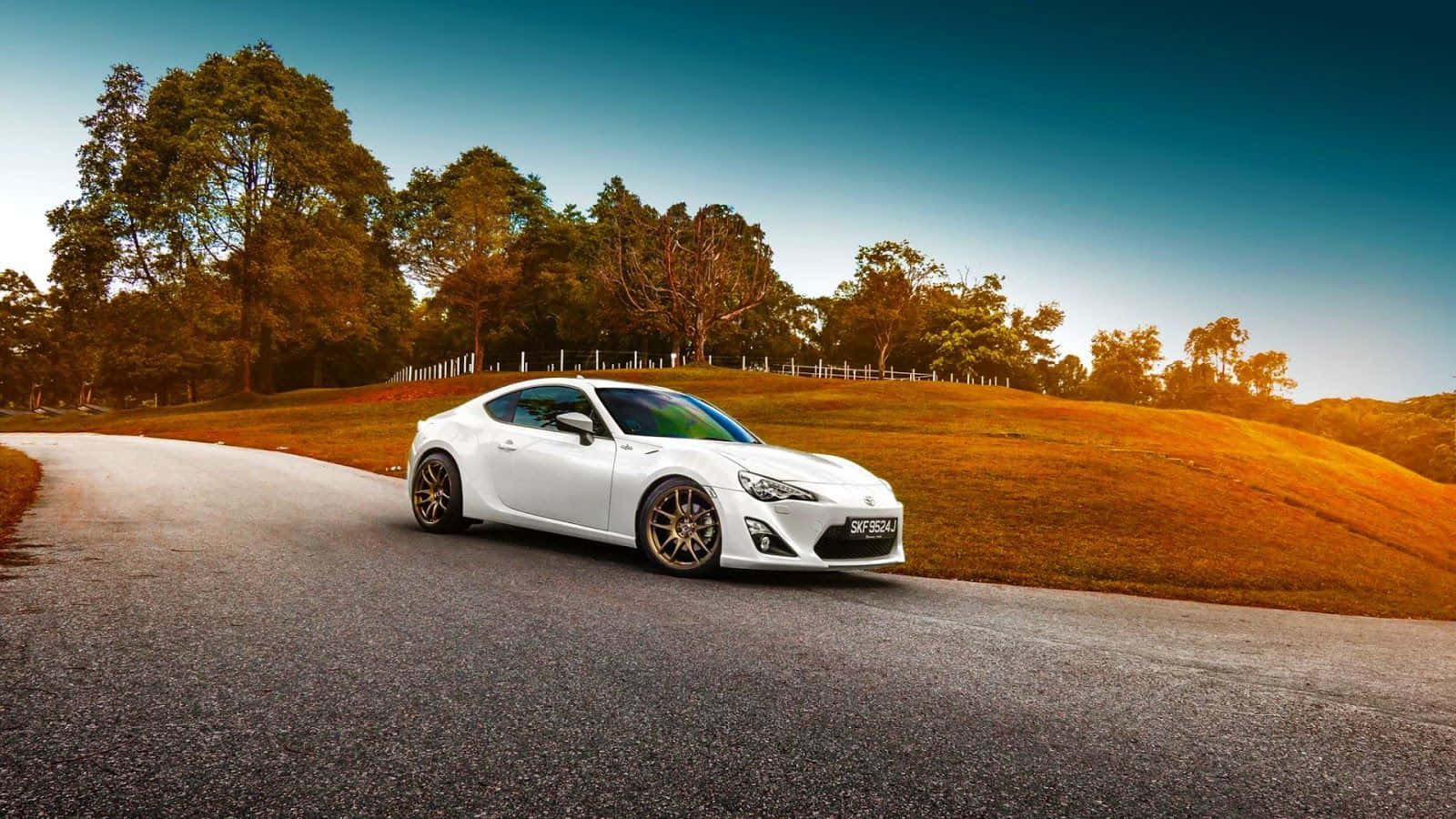 白色跑車在蜿蜒的道路上行駛，穿過日落時分的金色山丘。