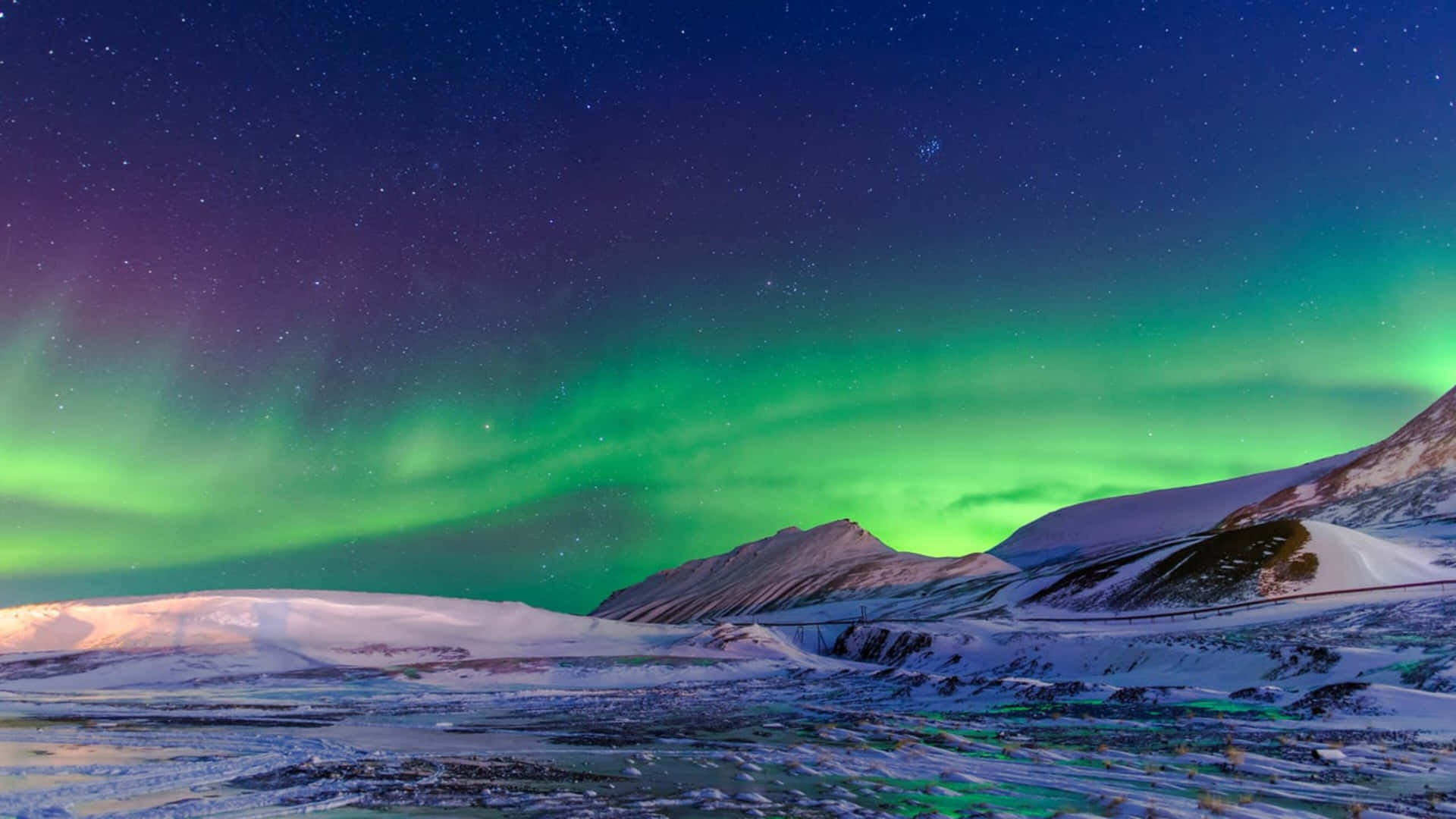 綠色北極光照亮星空下白雪覆蓋的山脈。