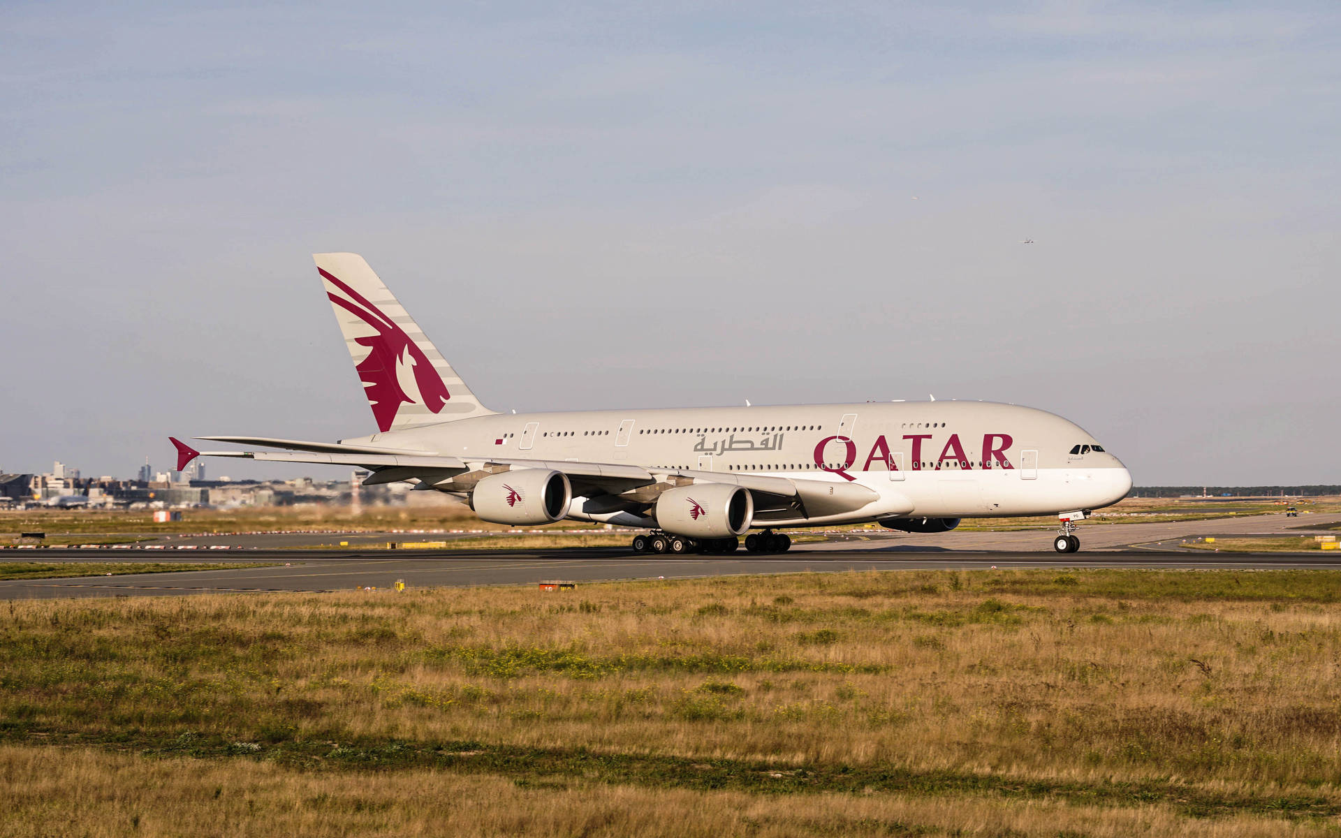 卡塔爾航空A380飛機在機場跑道上，背景有草和城市。 — 4K 飛機壁紙 壁紙