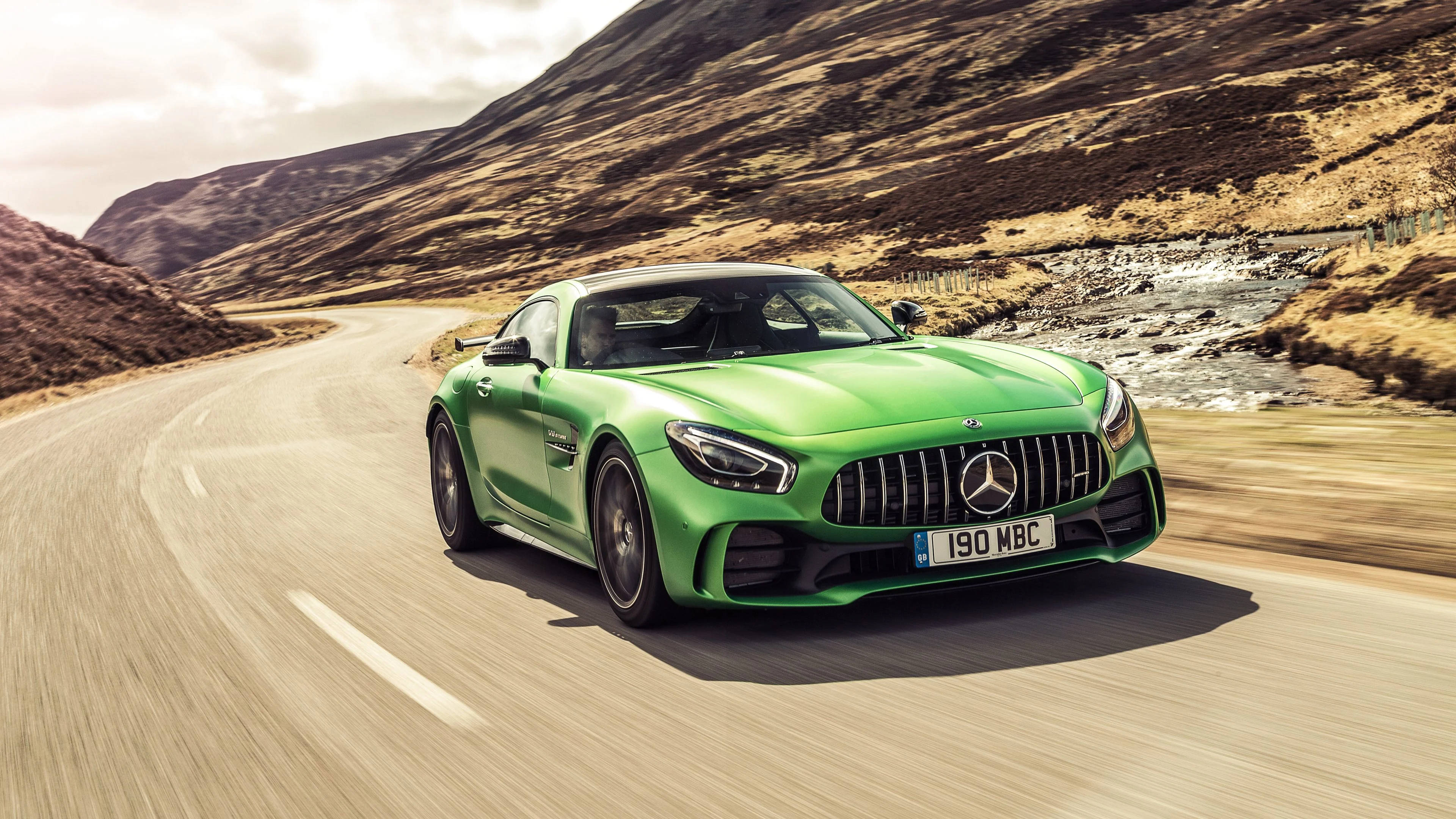 4K 奔馳 GTR AMG 壁紙 — 一輛充滿活力的綠色Mercedes-AMG GT R在蜿蜒的山路上飛馳，背景是崎嶇的山丘和一條河流。
