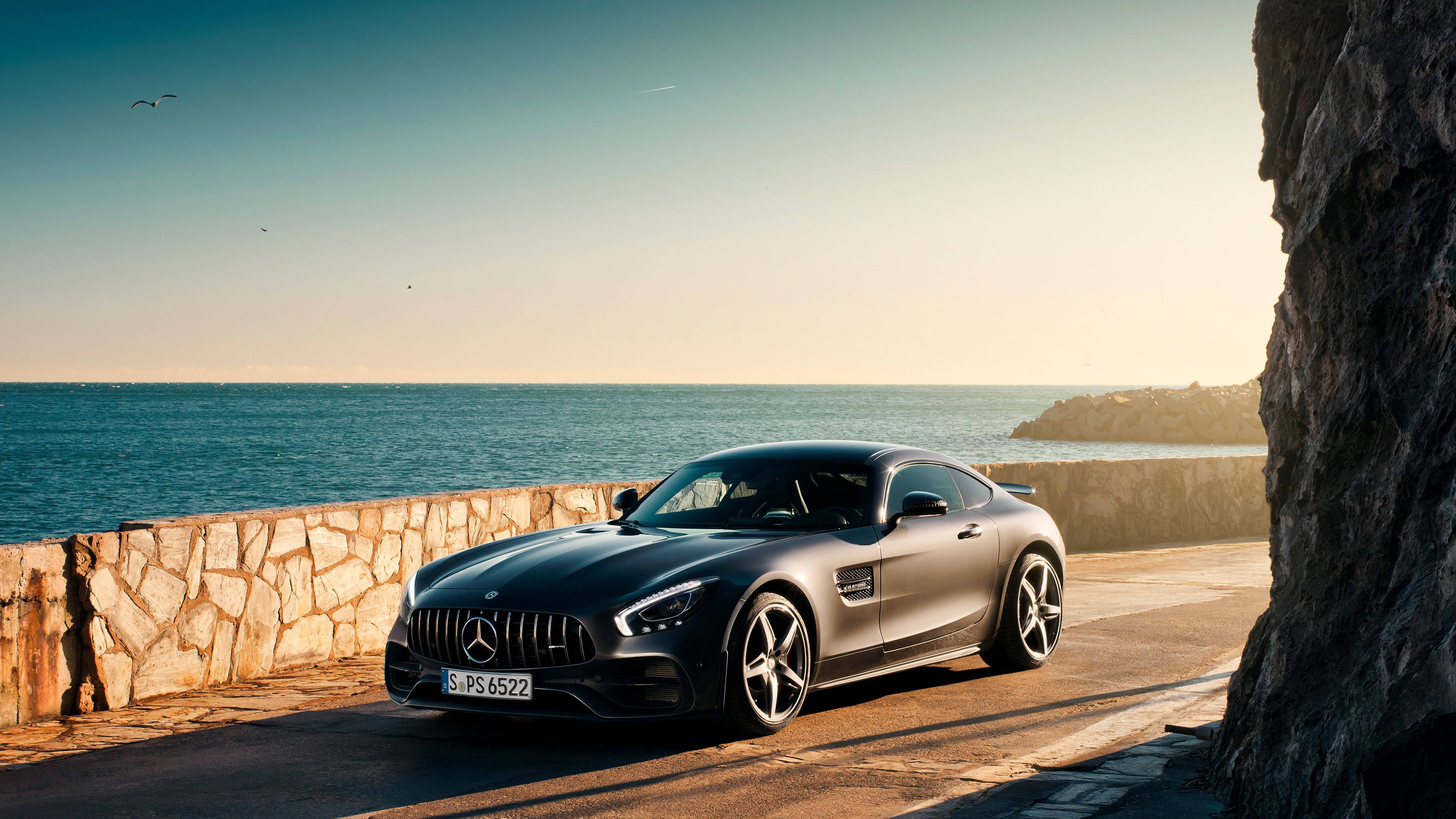 4K 奔馳海邊 壁紙 — 一架時尚的啞光黑色梅賽德斯-AMG GT跑車停泊在海邊的沿海公路上，正值黃金時段。