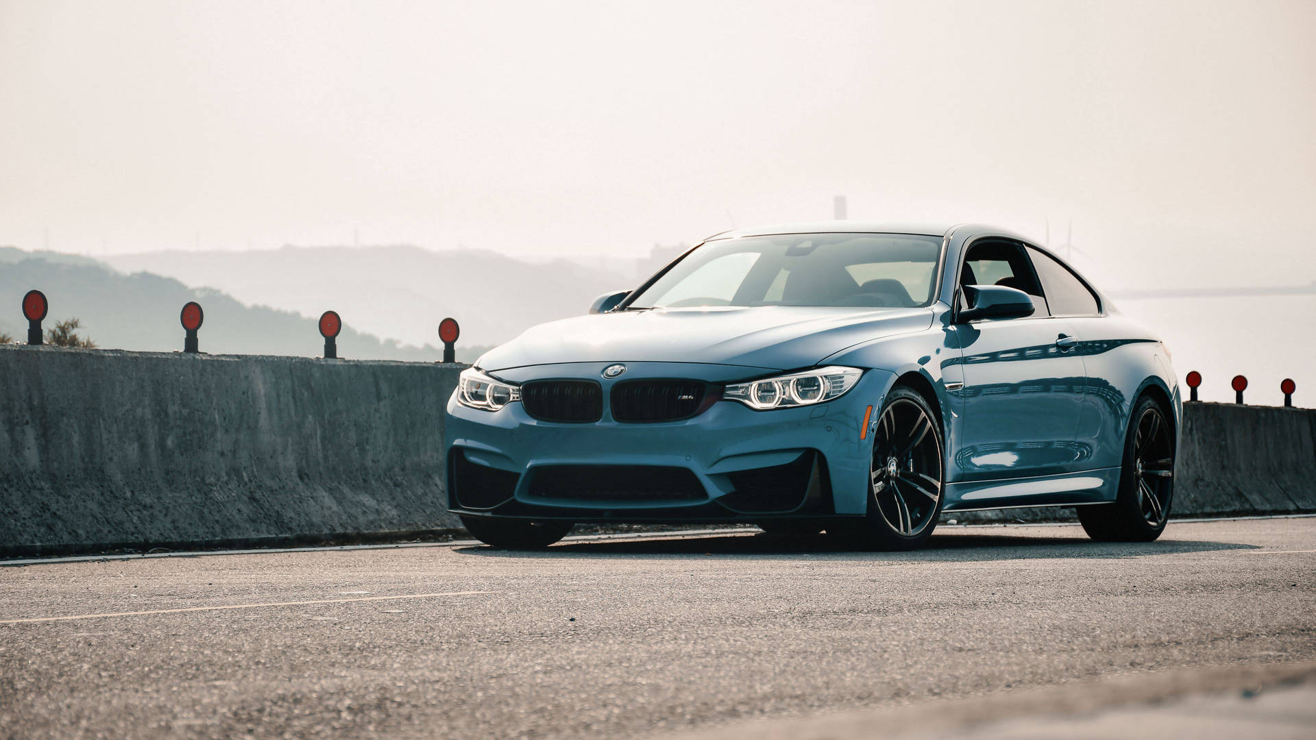 藍色BMW M4轎跑車停泊在沿海道路上，遠處有山丘。 — 4K BMW 壁紙 壁紙
