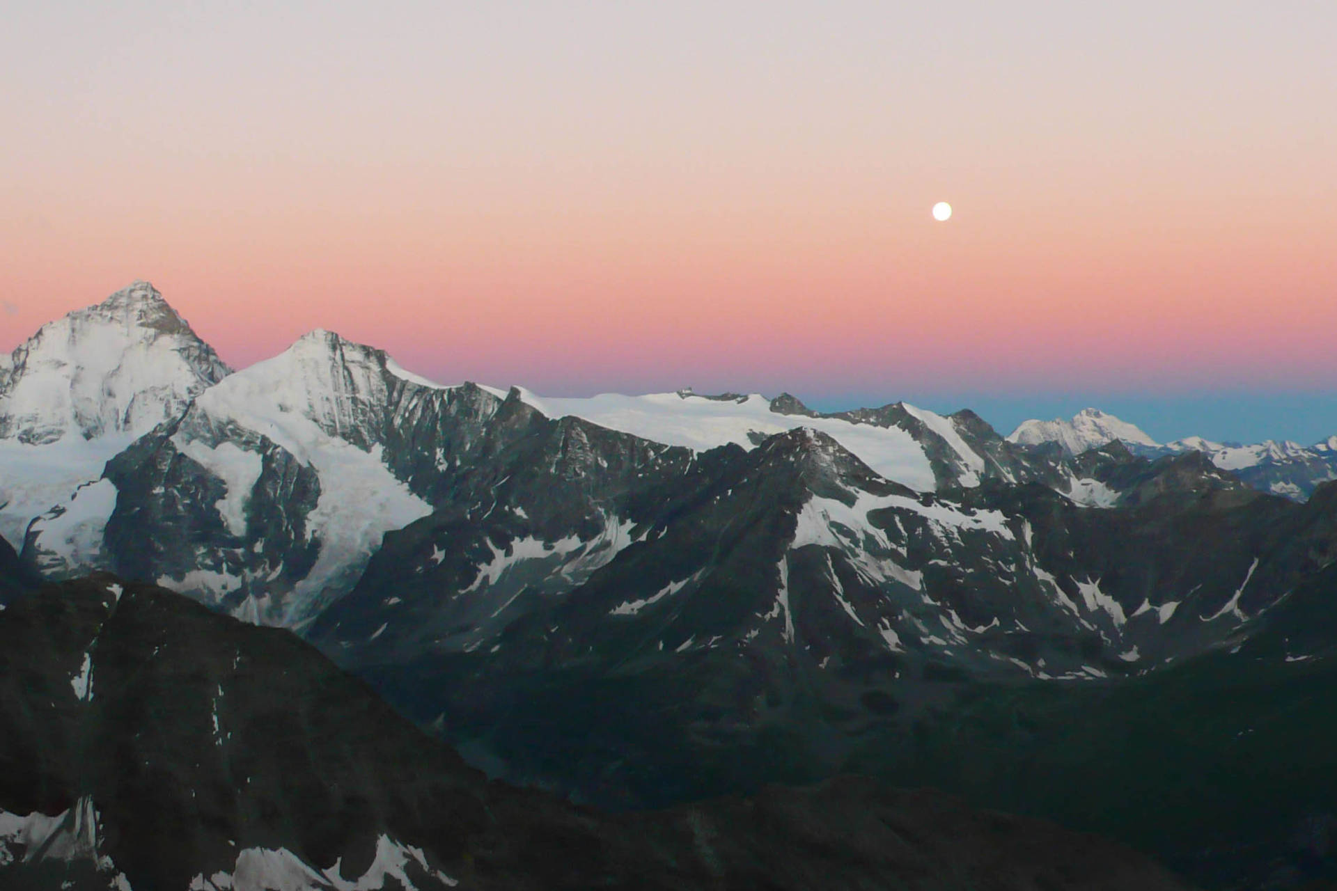 4K 山脈月景 壁紙 — 白雪覆蓋的山峰在柔和的粉紅和藍色暮色天空中聳立，上方有一輪明亮的月亮。