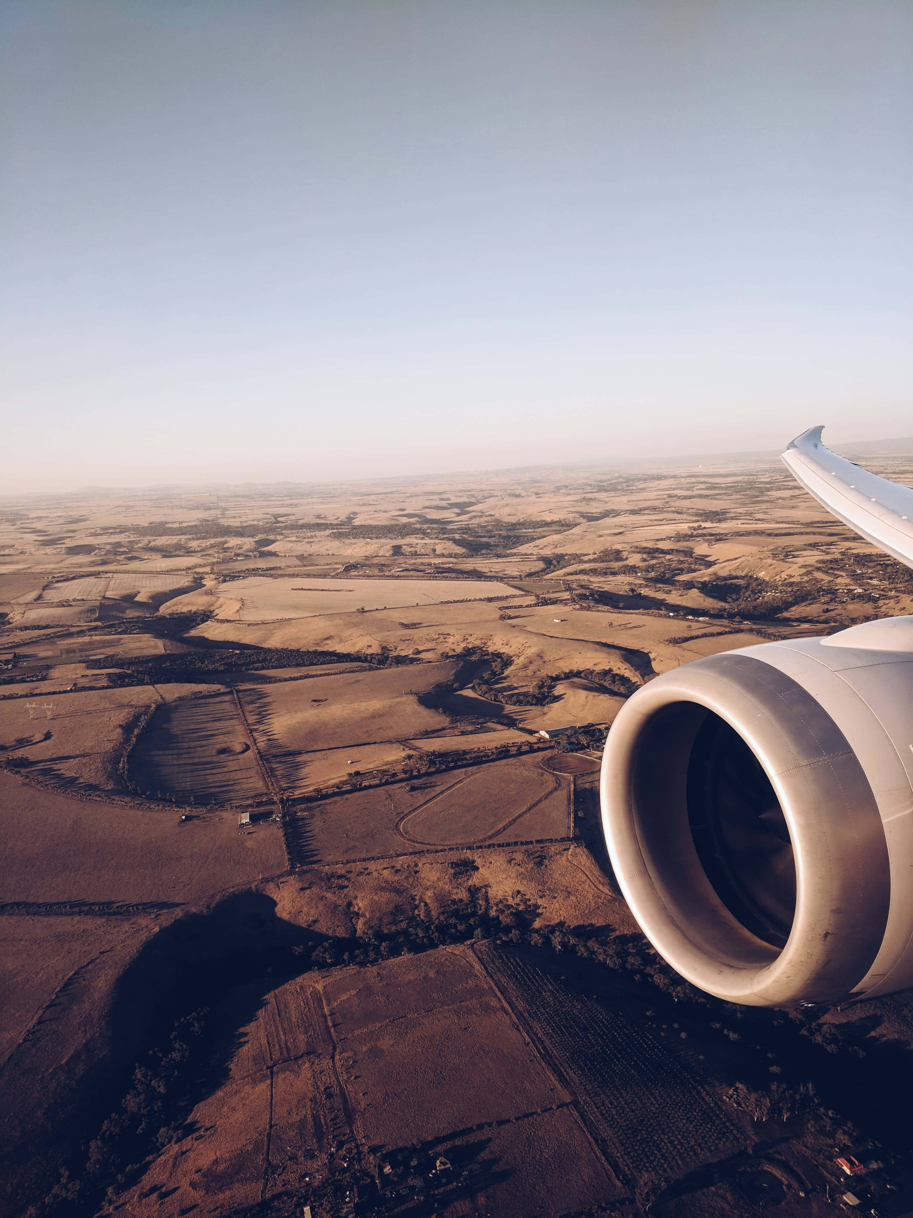 4K 微軟模擬飛行背景：飛機窗戶視角 壁紙 — 從飛機窗戶俯瞰的空中視角，顯示引擎和機翼在晴朗天空下的拼布農田之上。