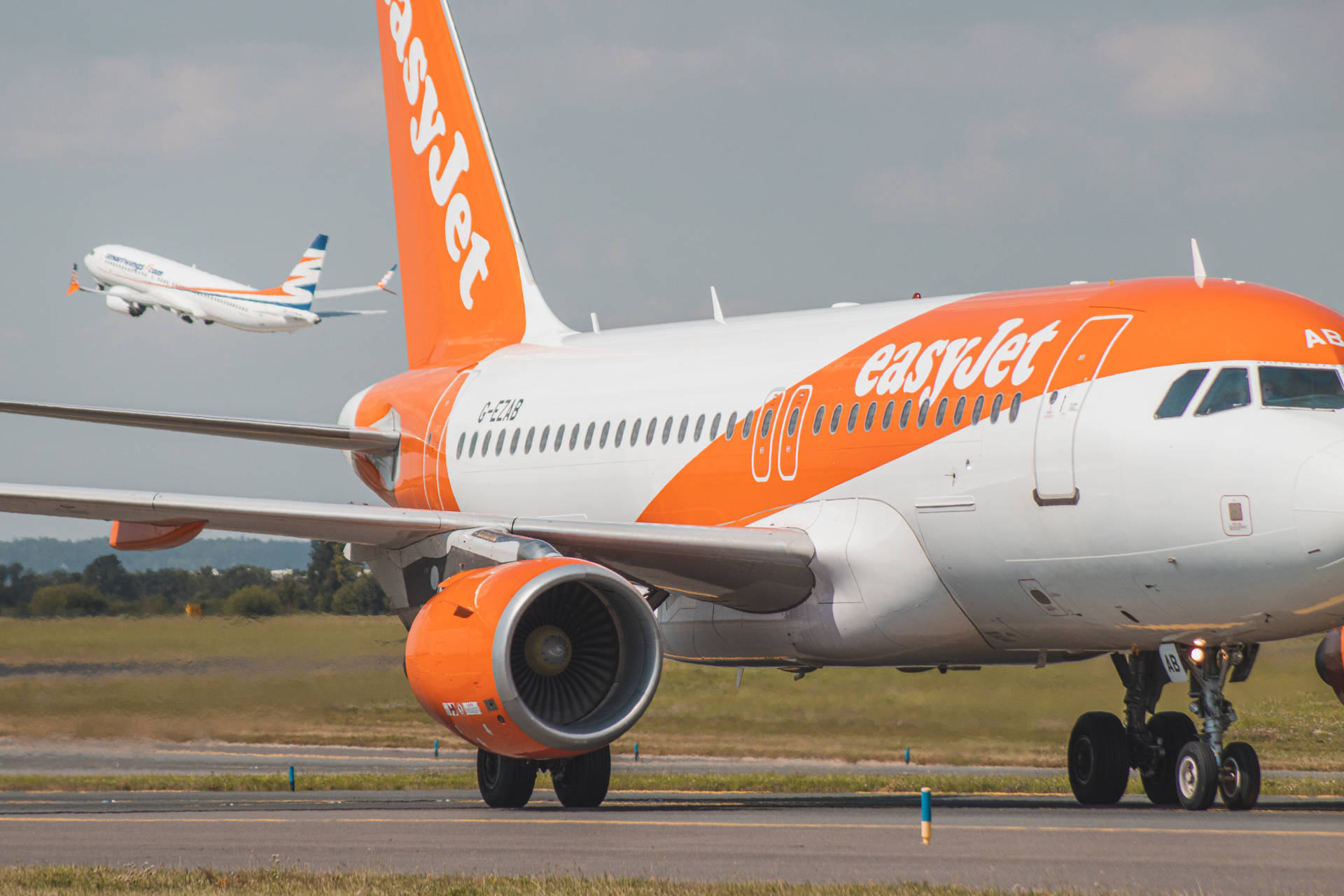 橙色和白色的易捷航空飛機在機場跑道上，背景有另一架飛機。 — 4K 飛機壁紙 壁紙