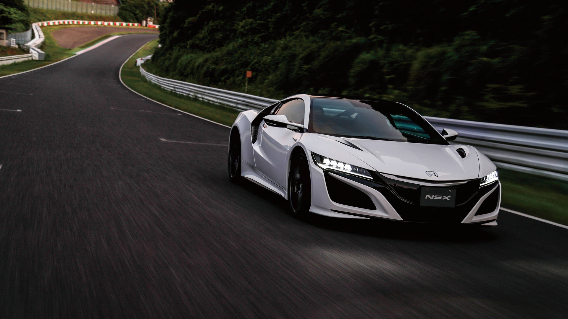 白色Acura NSX在綠樹環繞的彎路上飛馳。