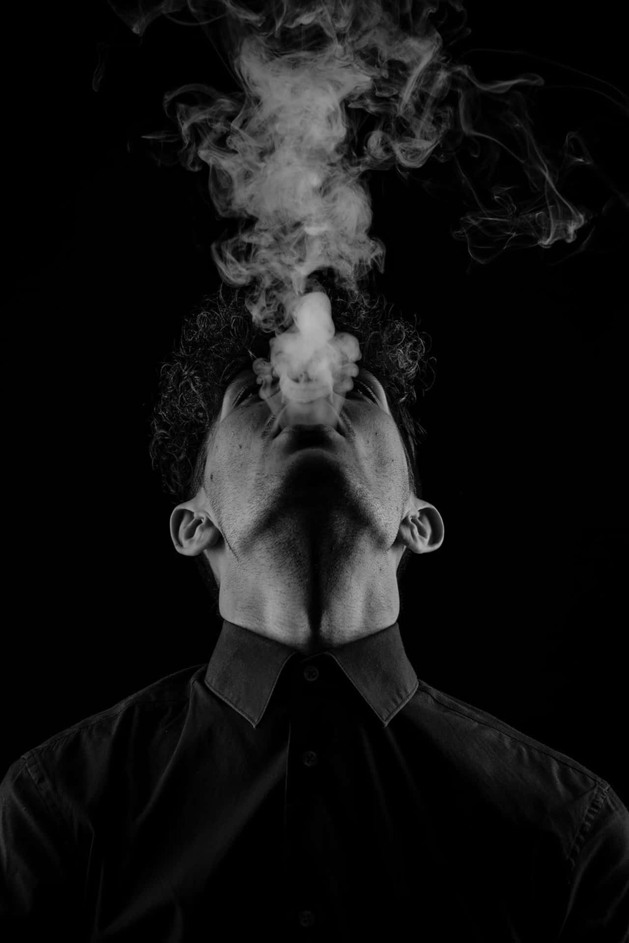 一個男人在黑白工作室肖像中向上呼出煙霧。