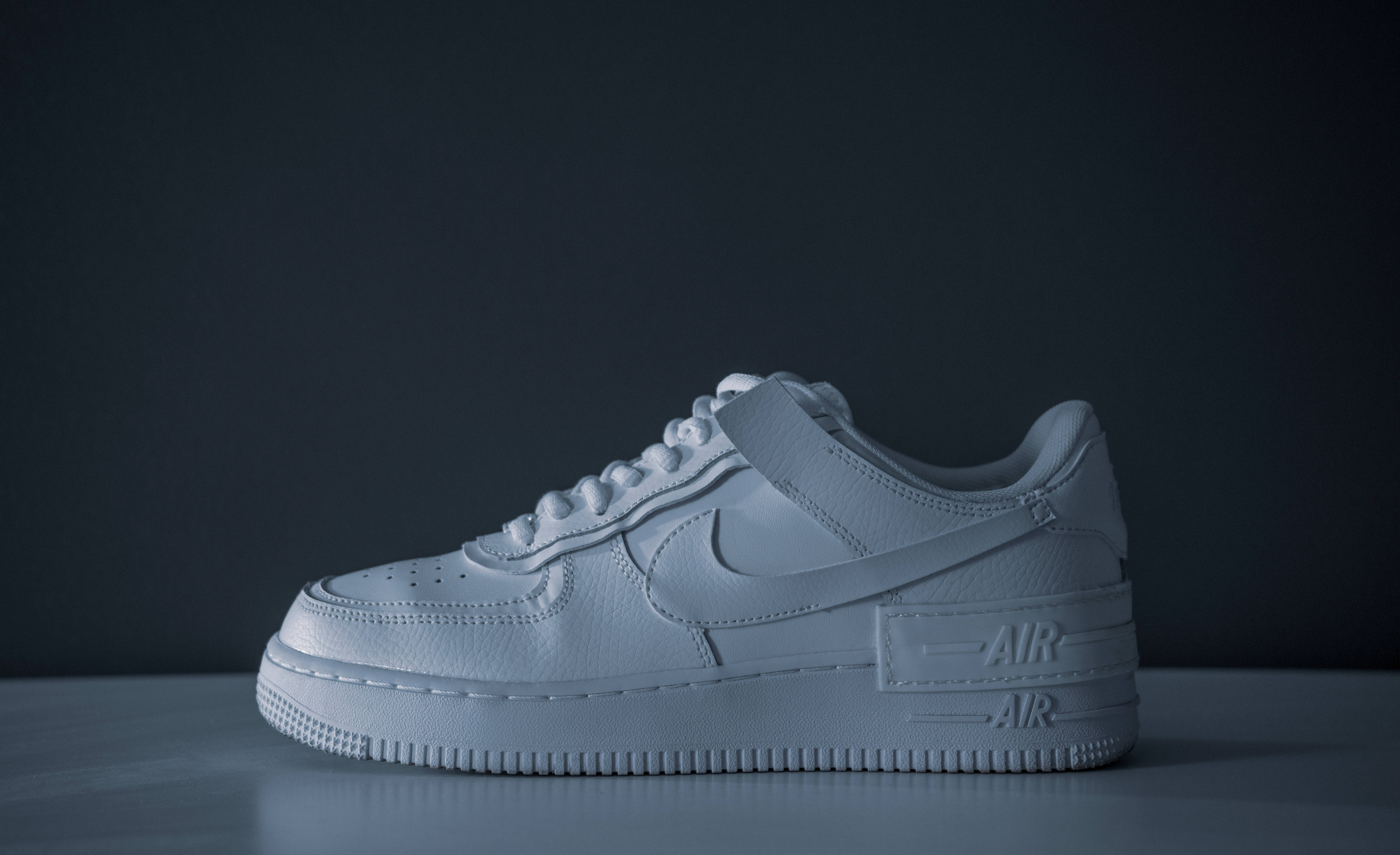 4K 白色耐克Air鞋配黑色背景 壁紙 — 一隻單色白色Nike Air Force 1波鞋孤立地放在灰色表面上，背景為深色。