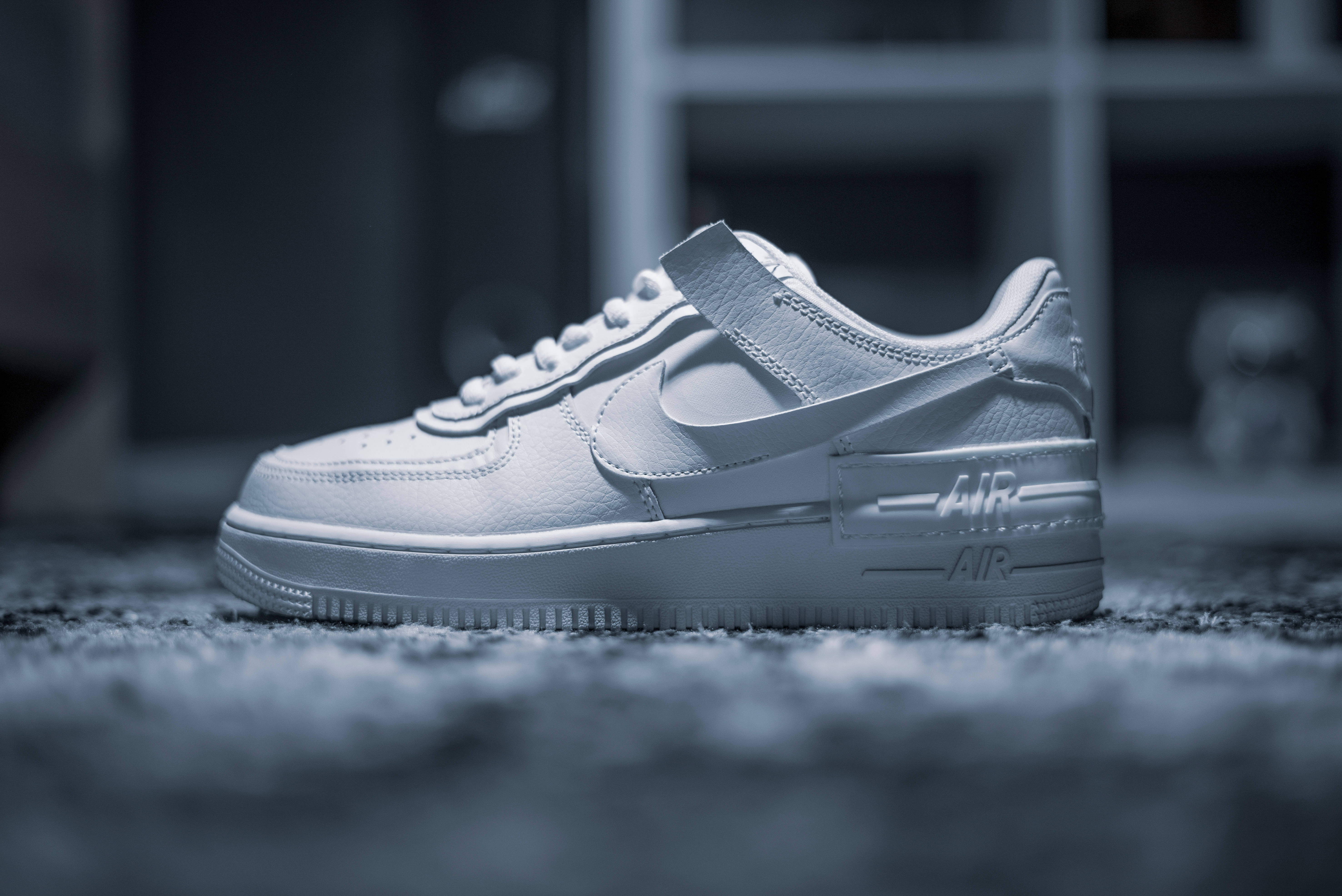 4K 白色耐克鞋在地毯上 壁紙 — 一雙純白色的Nike Air Force 1運動鞋放在有紋理的地毯上，背景是模糊的室內環境。