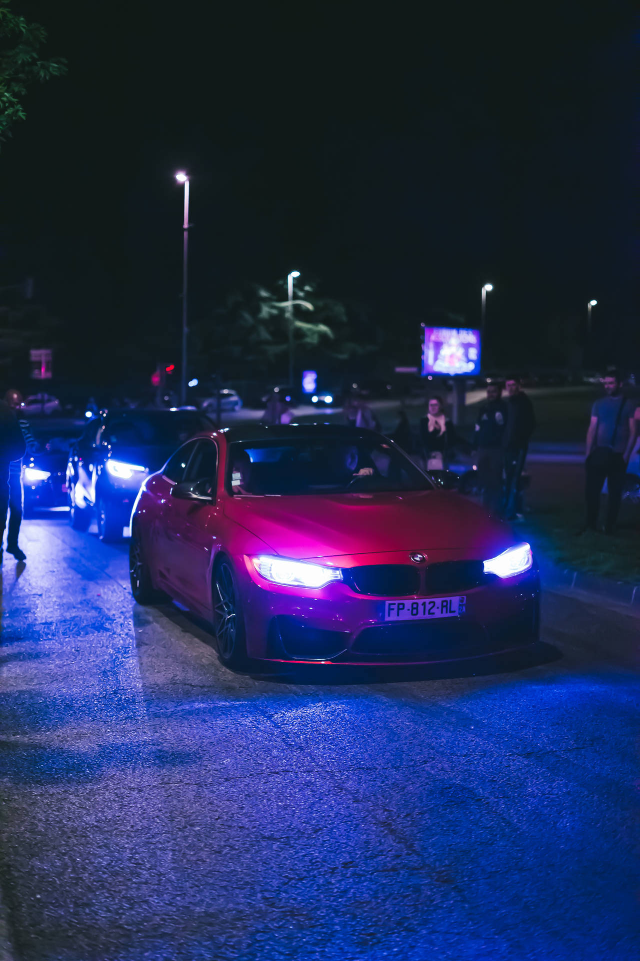 粉紅色跑車，車頭燈明亮，停在夜晚濕漉漉的街道上，附近有人。 — 4K BMW 壁紙 壁紙