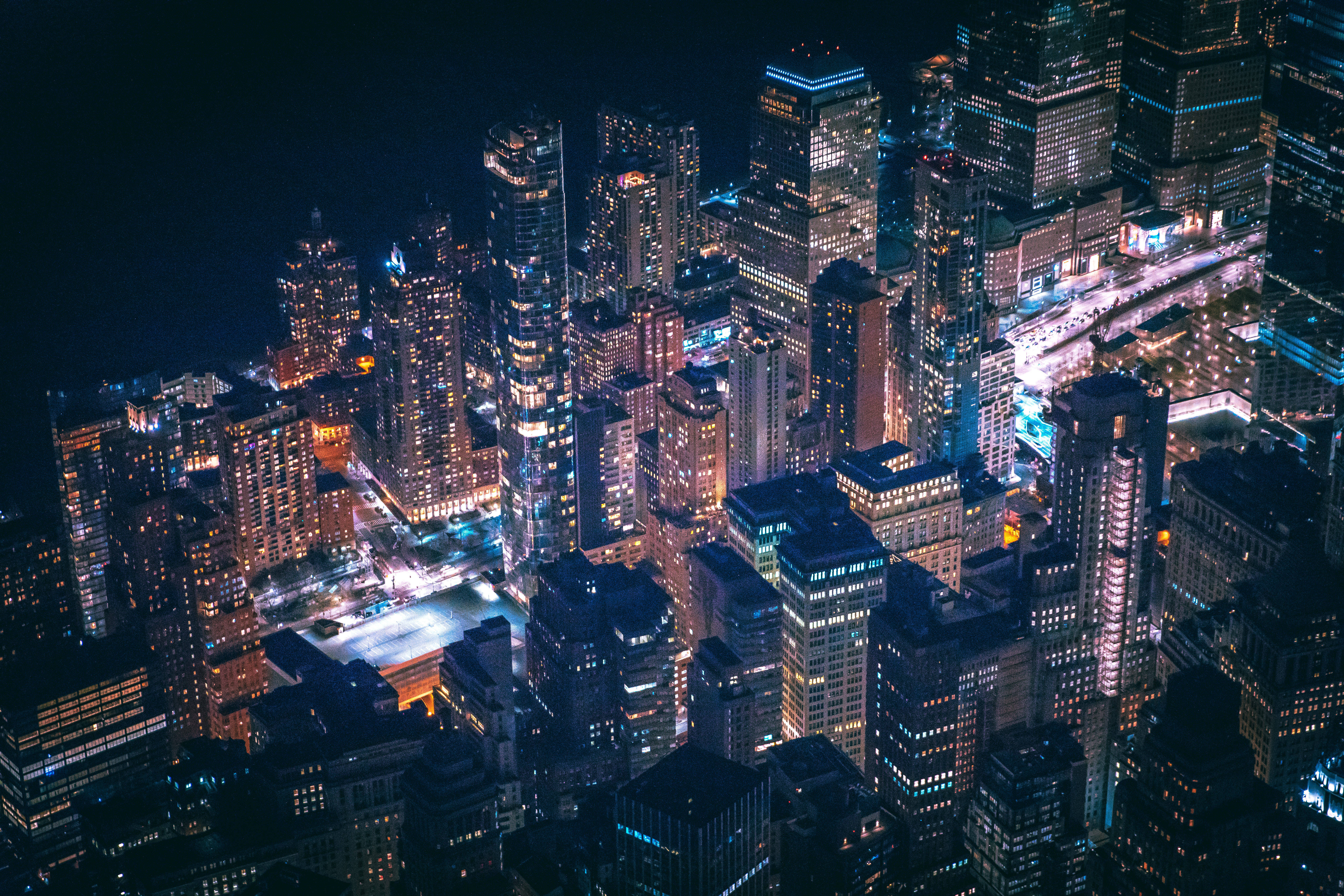 4K 紐約市夜景燈光 壁紙 — 密集城市景觀的鳥瞰圖，夜晚高聳的摩天大樓在黑暗的天空中閃爍著溫暖與冷色調的光芒。