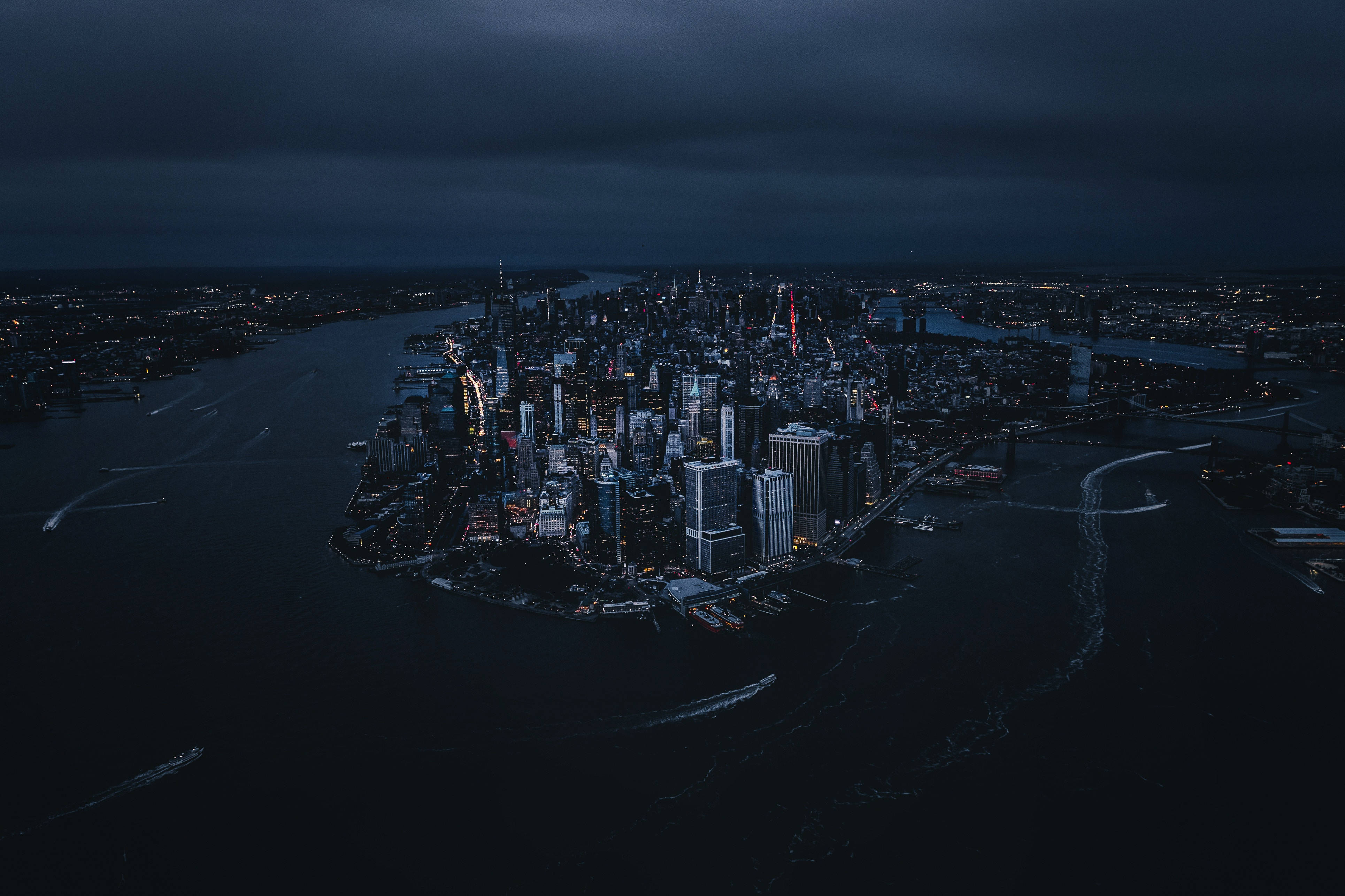 4K 紐約市夜間探險 壁紙 — 暴風雨天空下，閃爍摩天大樓與黑暗水域的廣闊城市夜景鳥瞰圖。