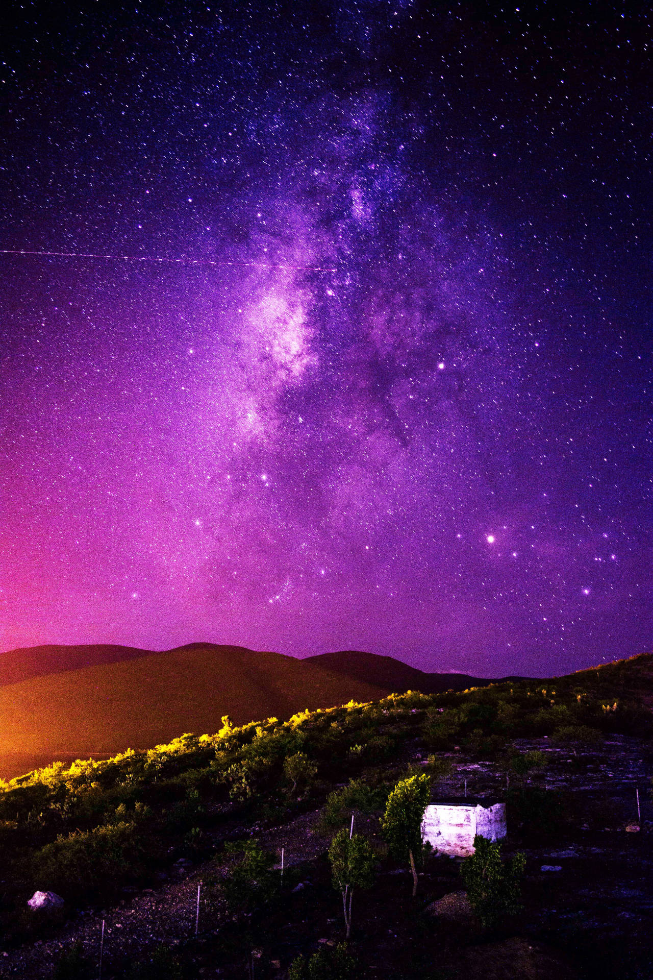 在充滿活力的紫色星空下，背景是山丘，一個發光的石結構。 — 蘋果 壁紙