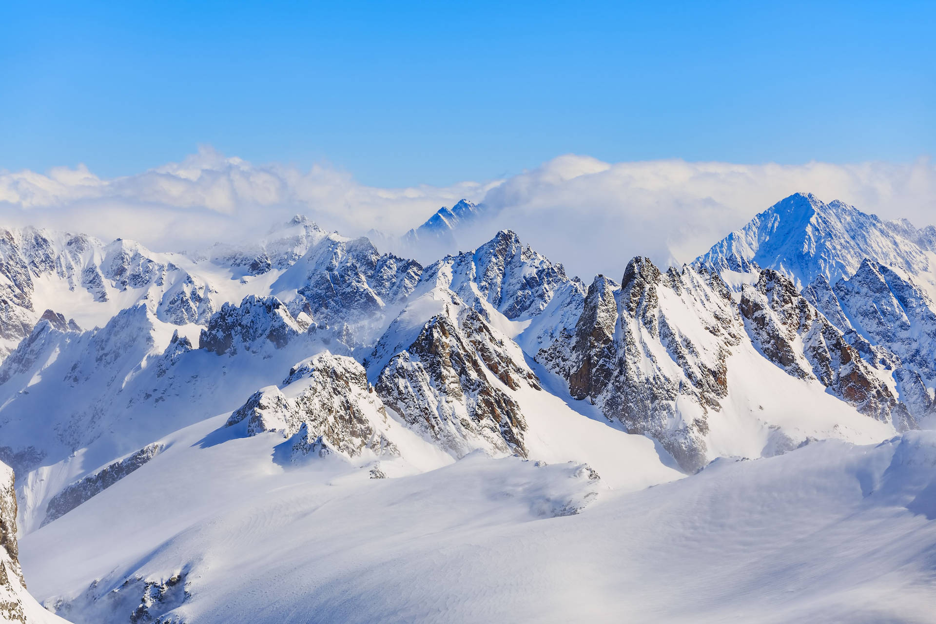 積雪的山脈在清澈藍天下，尖銳的山峰聳立於雲層之上。