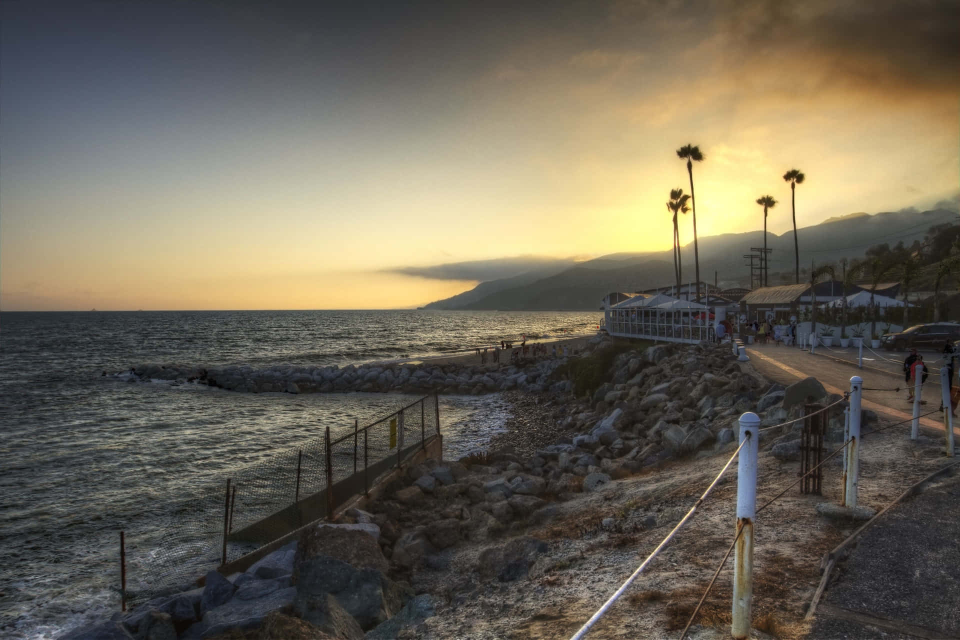 日落時分的海岸小徑，背景有棕櫚樹和山巒