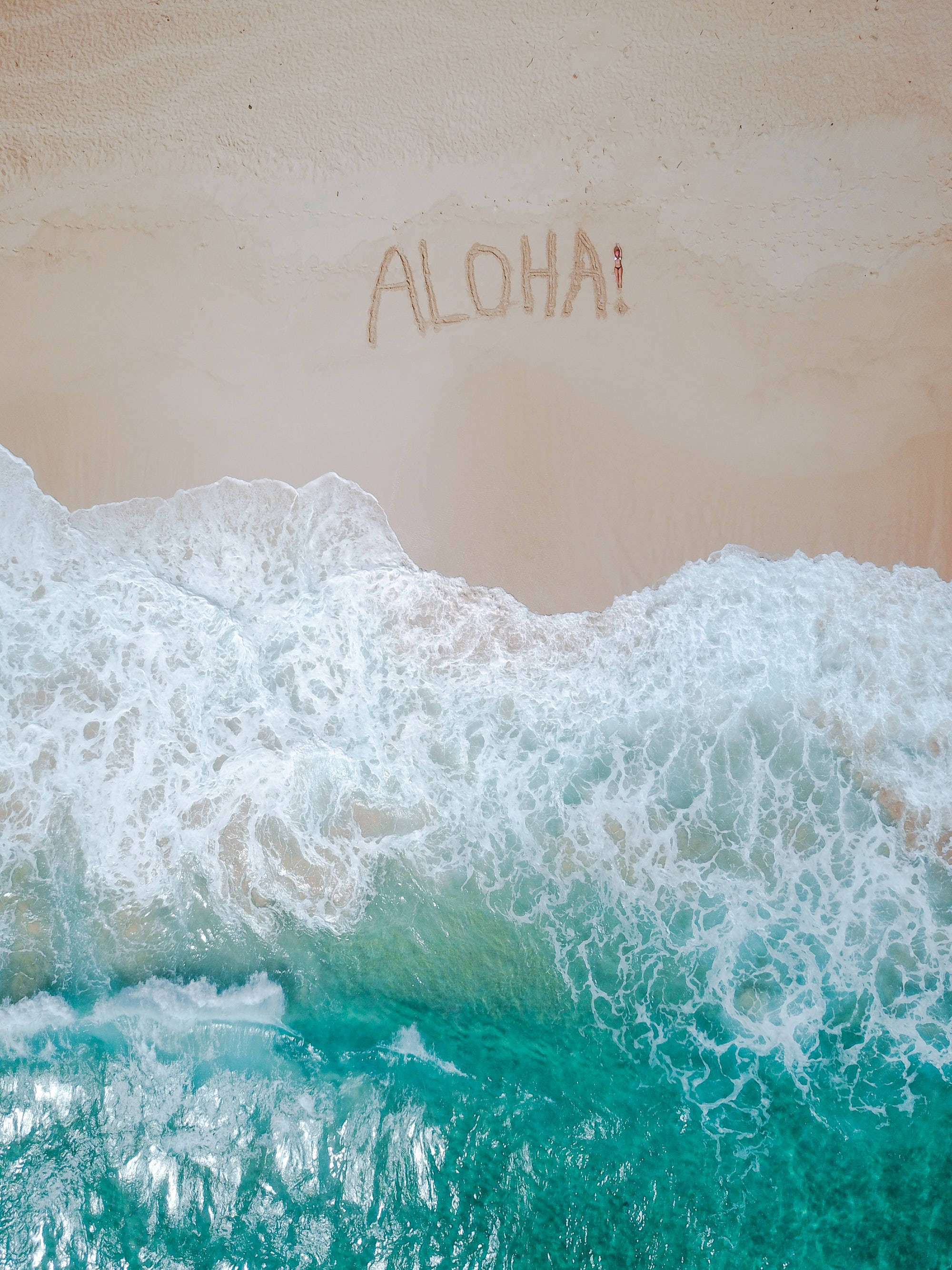 4K 超高清 海灘ALOHA 壁紙 — 從高空俯瞰，碧綠色的海浪拍打著沙灘，沙灘上寫有「ALOHA！」字樣。