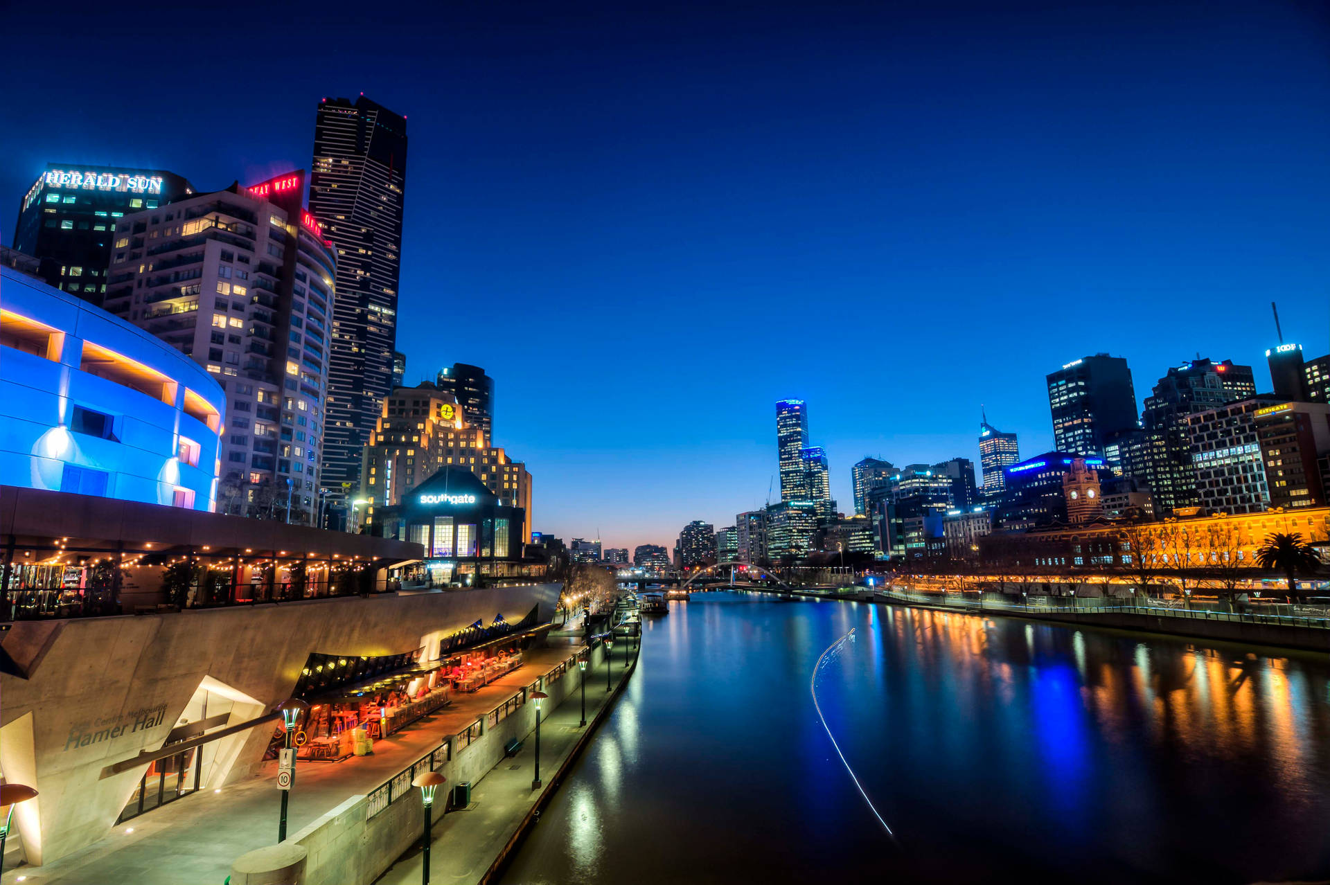 黃昏時分的城市天際線，燈火通明的建築物和河流倒影。