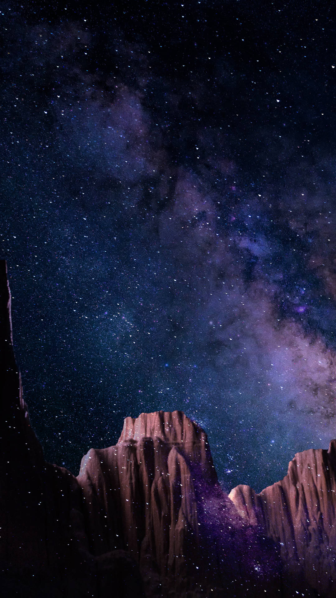 4K 超高清宇宙壯麗視野 壁紙 — 一個充滿星星和紫色星雲的壯麗夜空，拱形籠罩在崎嶇的深色岩石地貌之上。