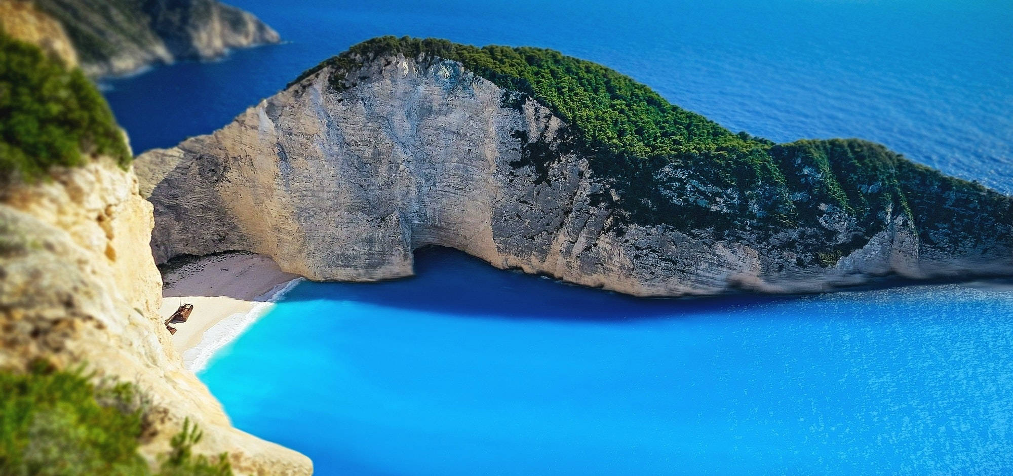 4K 超高清海灘山丘 壁紙 — 納瓦吉奧海灘的壯麗景色，碧綠的海水被高聳的白色懸崖環抱，懸崖上覆蓋著茂密的綠植。