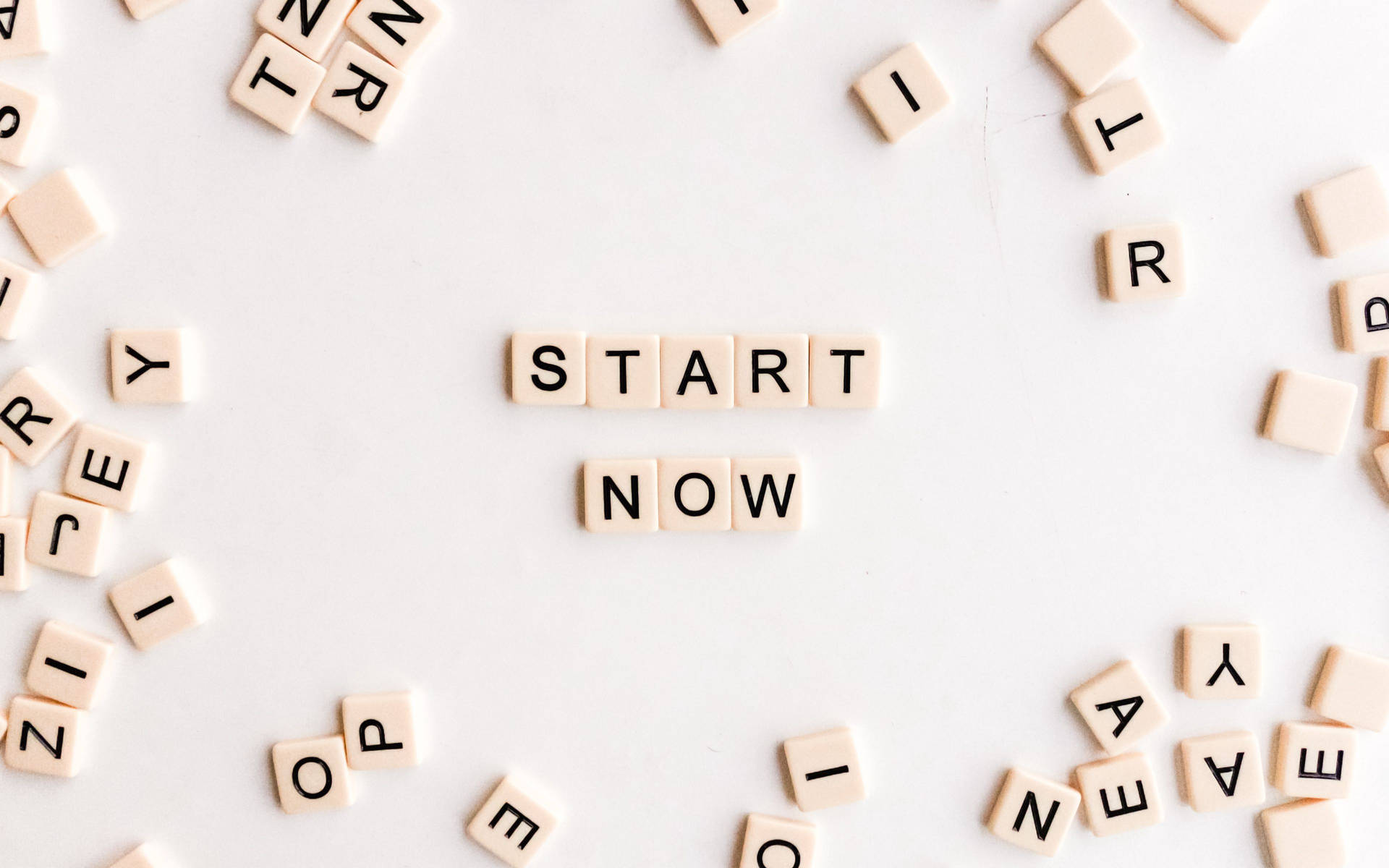 散落的字母瓷磚在白色表面上形成 'START NOW' 這個短語。