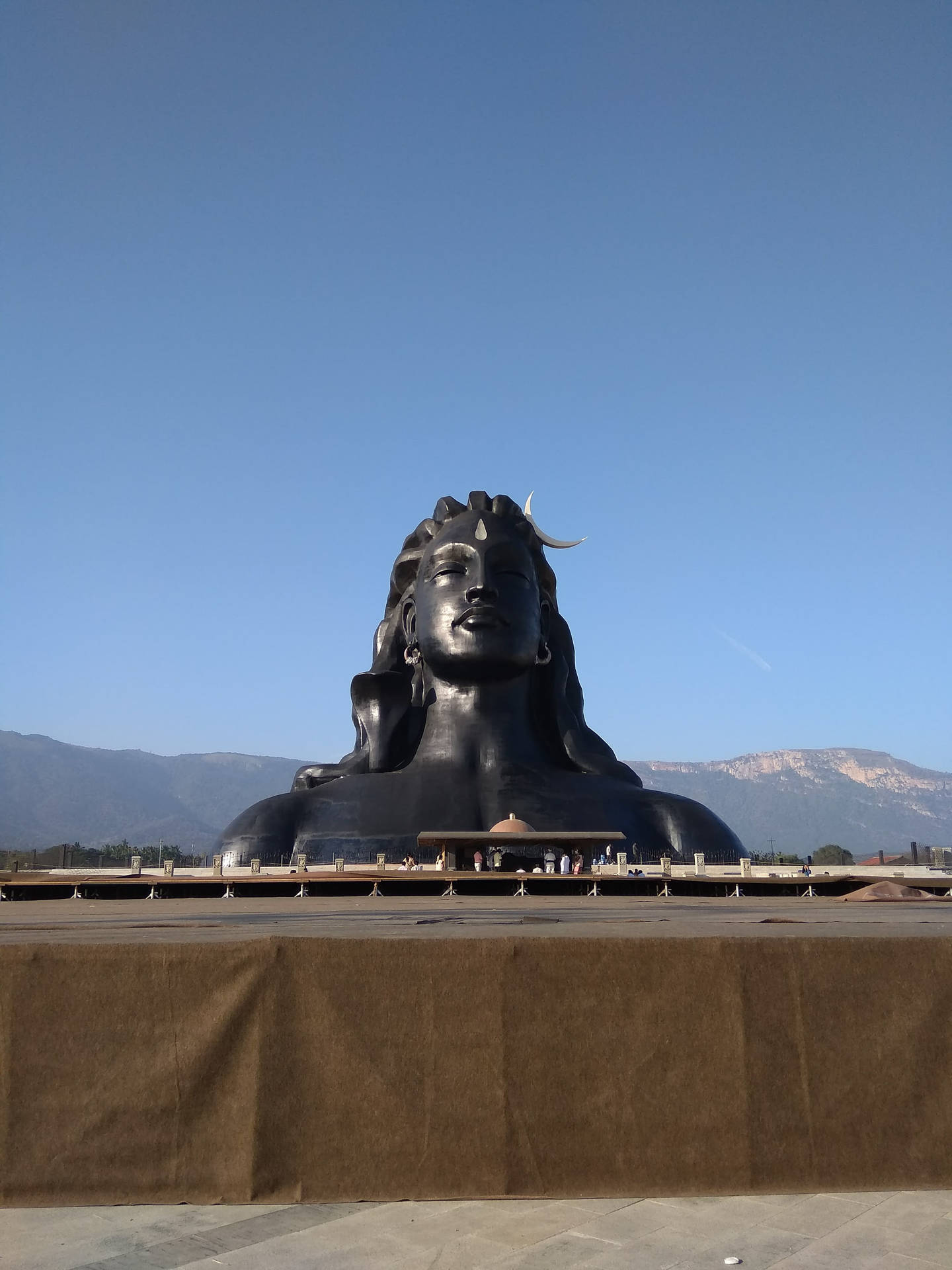 巨大的黑色濕婆神像，新月形頭髮，以藍天和山脈為背景。