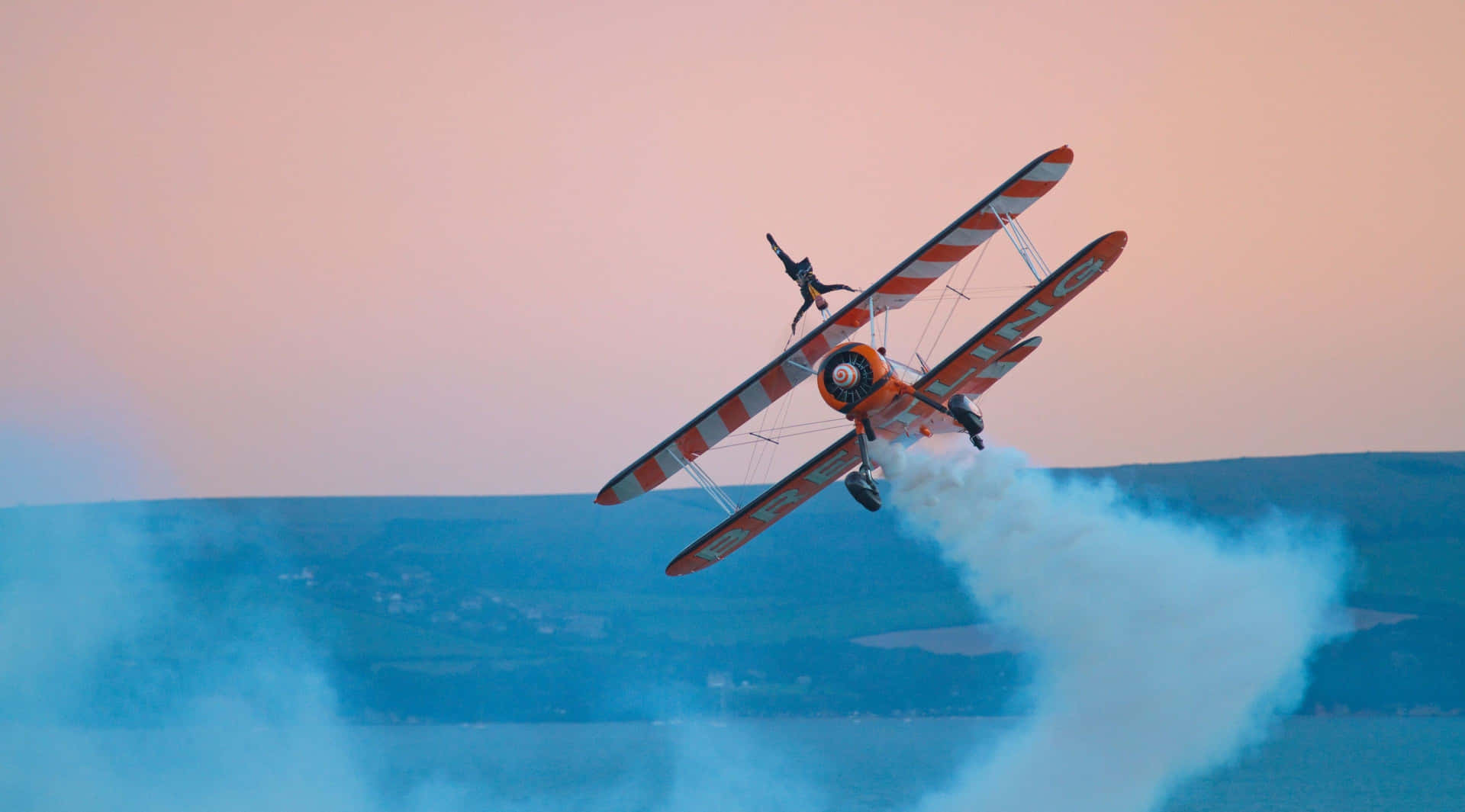 紅白雙翼飛機在日落時低飛過湖泊，留下煙跡。