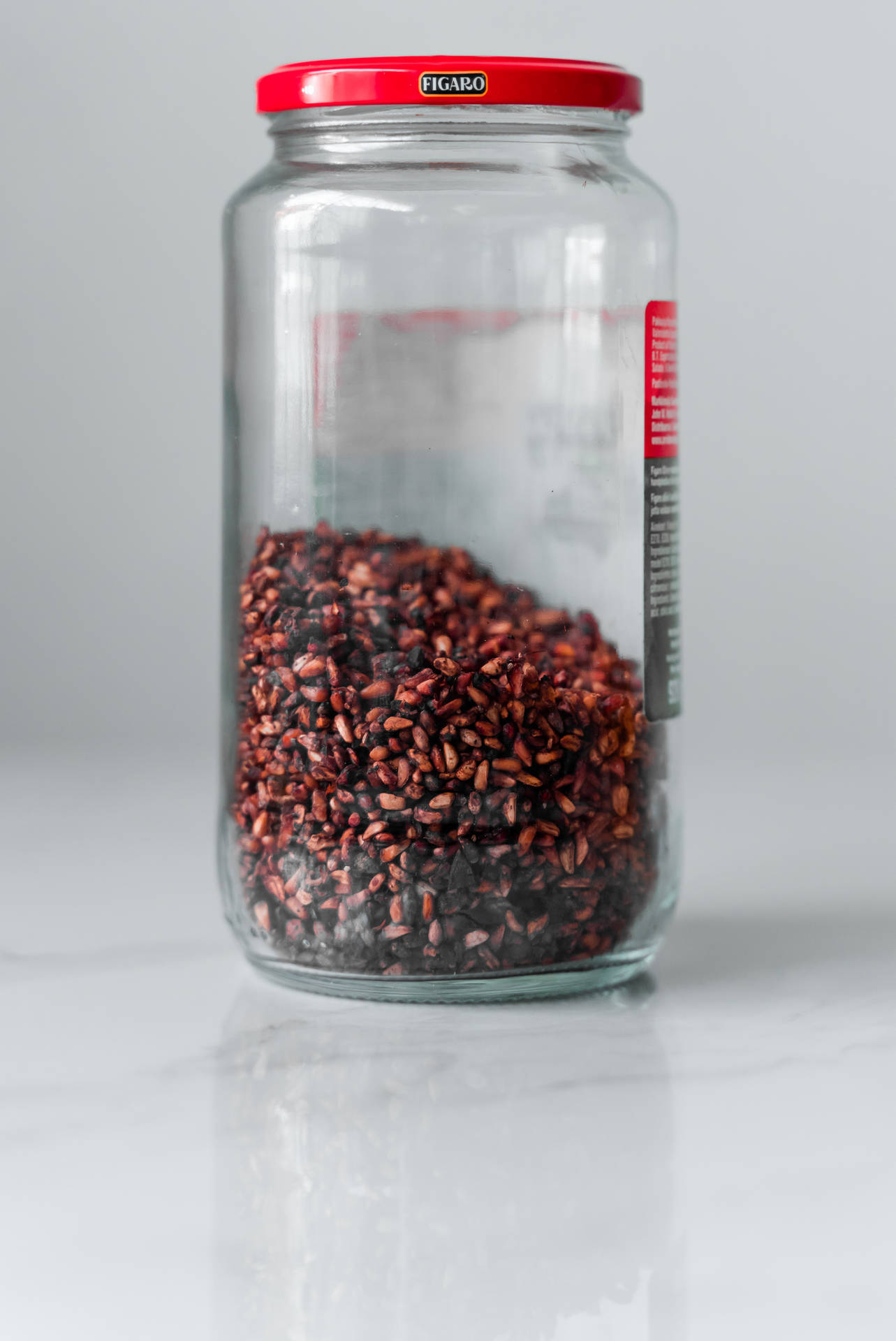 玻璃罐裝滿紅米和黑米，放在白色大理石表面上。