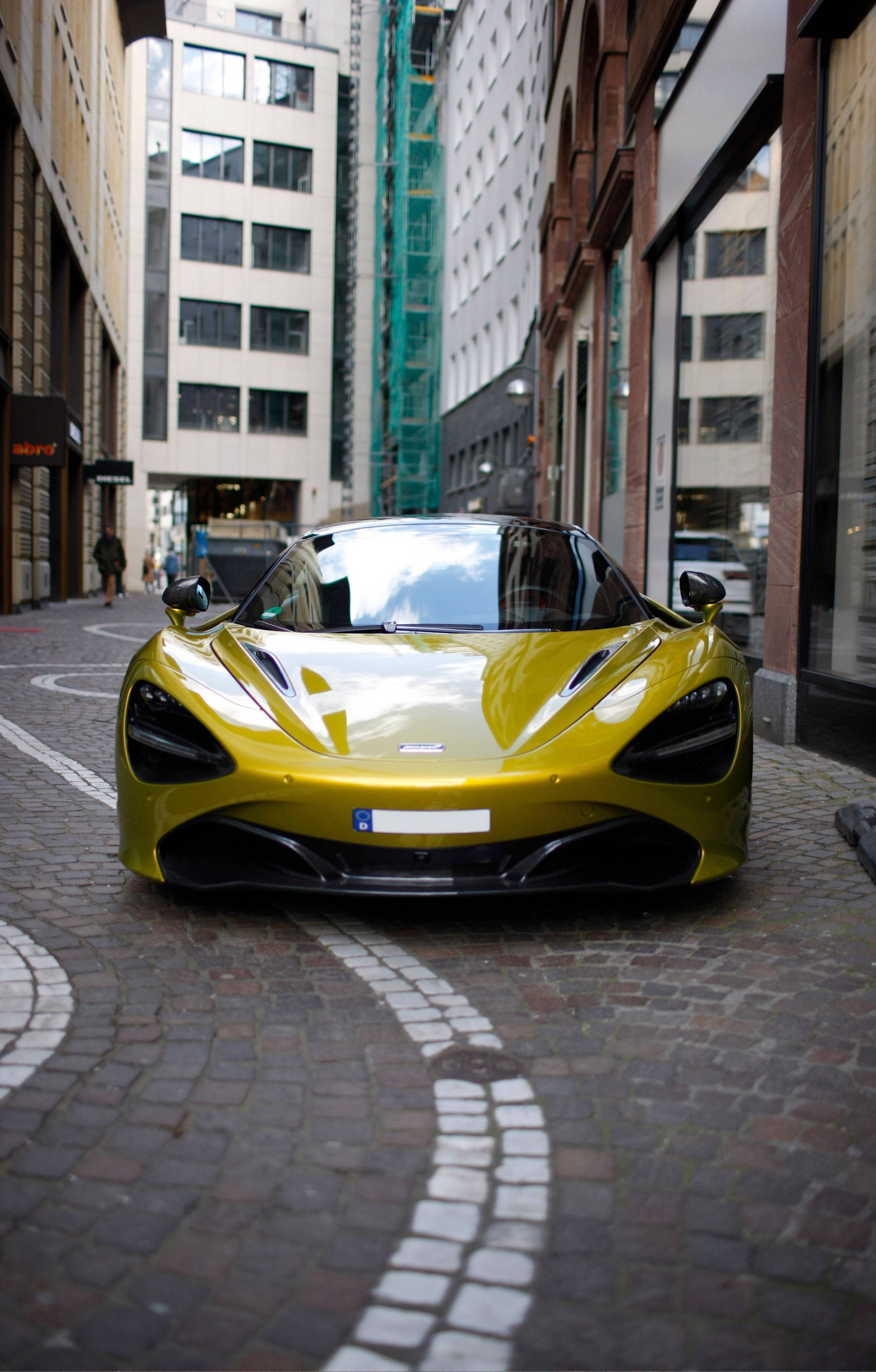 以全新4K蘭博基尼iPhone領先潮流 壁紙 — 一輛鮮黃色McLaren跑車停泊在鵝卵石街道上，兩旁是高聳的城市建築。
