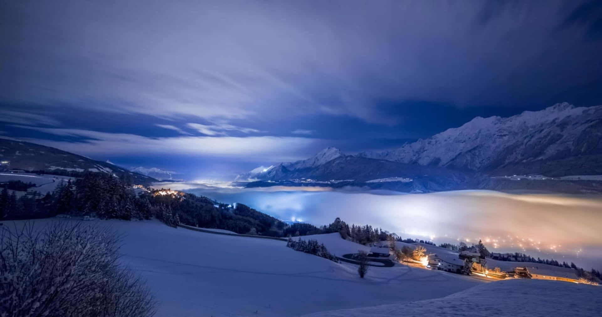 夜晚白雪覆蓋的山谷，村莊燈光在黑暗雲層下閃爍。