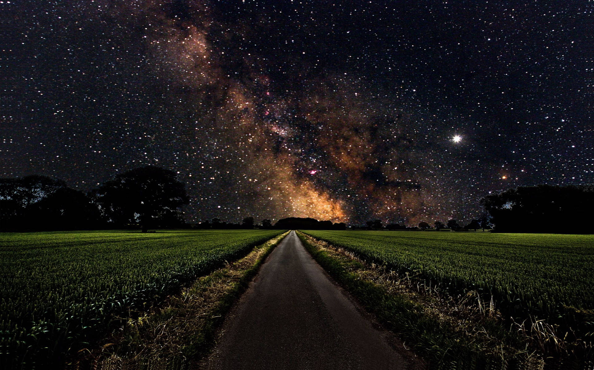 一條道路穿過田野，在星空下，銀河系清晰可見。 — 4K太空 壁紙