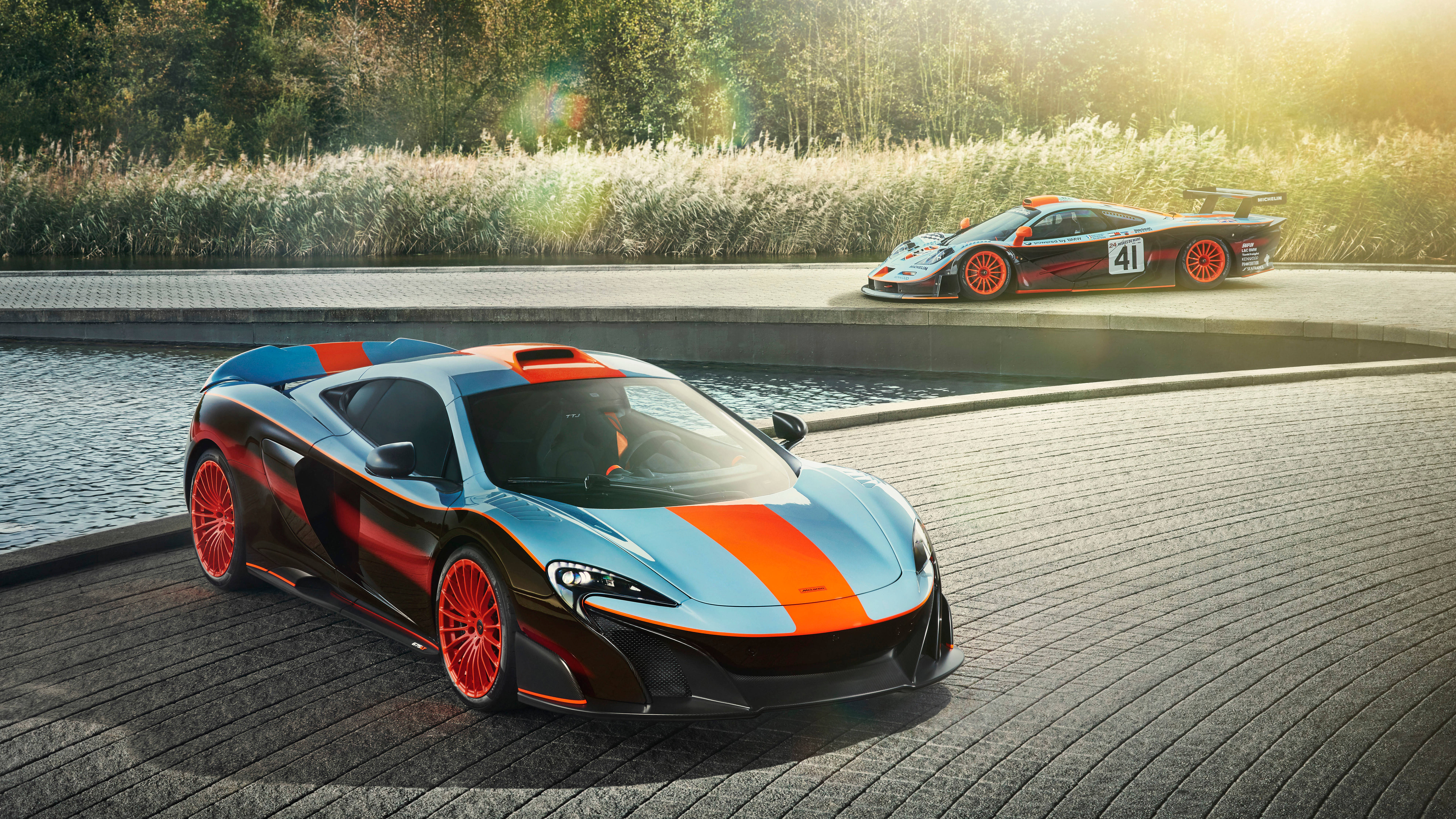 4K橙銀色跑車水畔停泊 壁紙 — 兩輛線條流暢的McLaren超級跑車帶有醒目的橙色條紋，在金色陽光下於水邊的木製碼頭上閃閃發光。