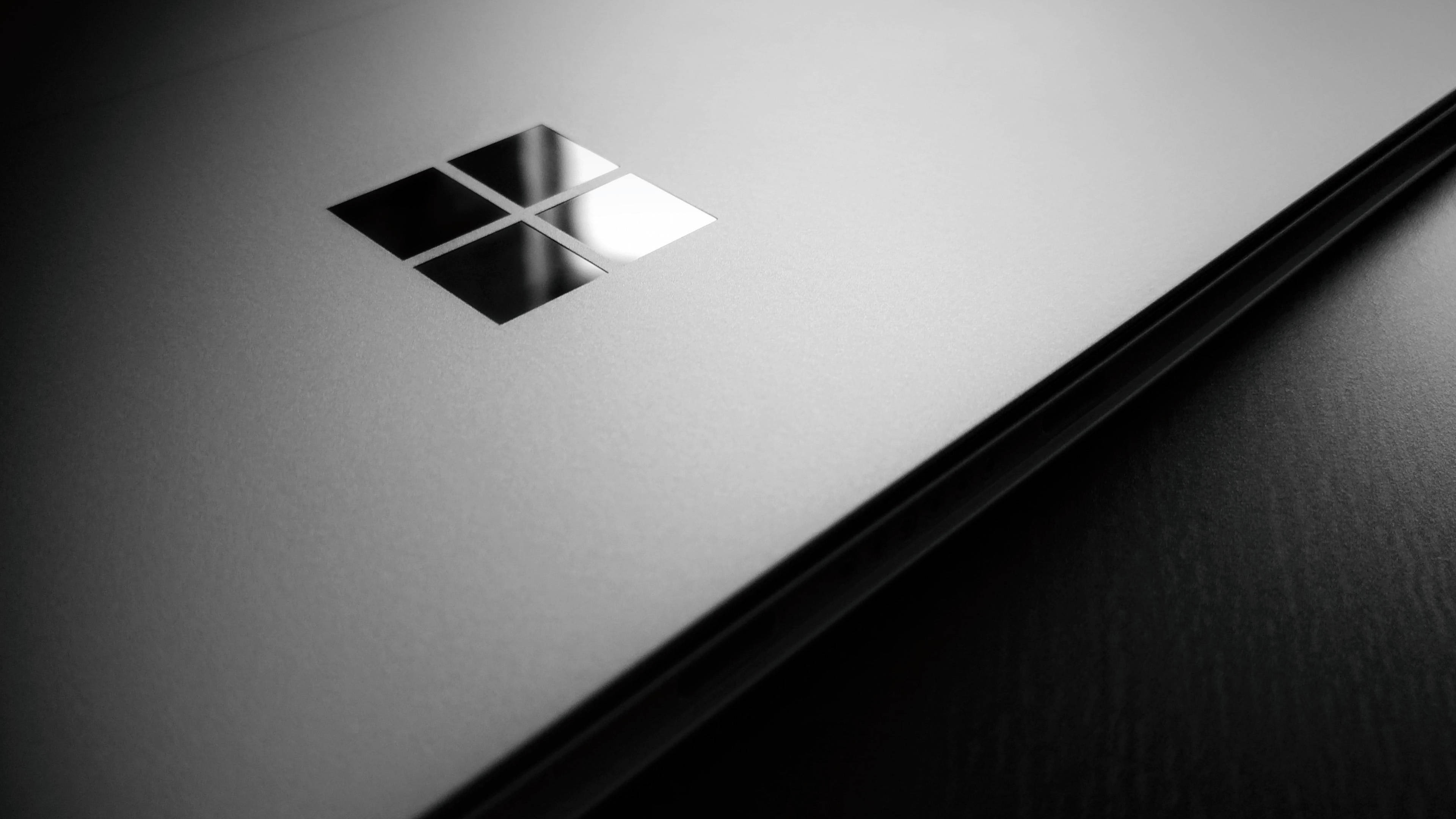 4K筆電 Windows 標誌 壁紙 — 在戲劇性的工作室燈光下，一個時尚的黑色筆記本電腦蓋，帶有反光的Microsoft標誌。