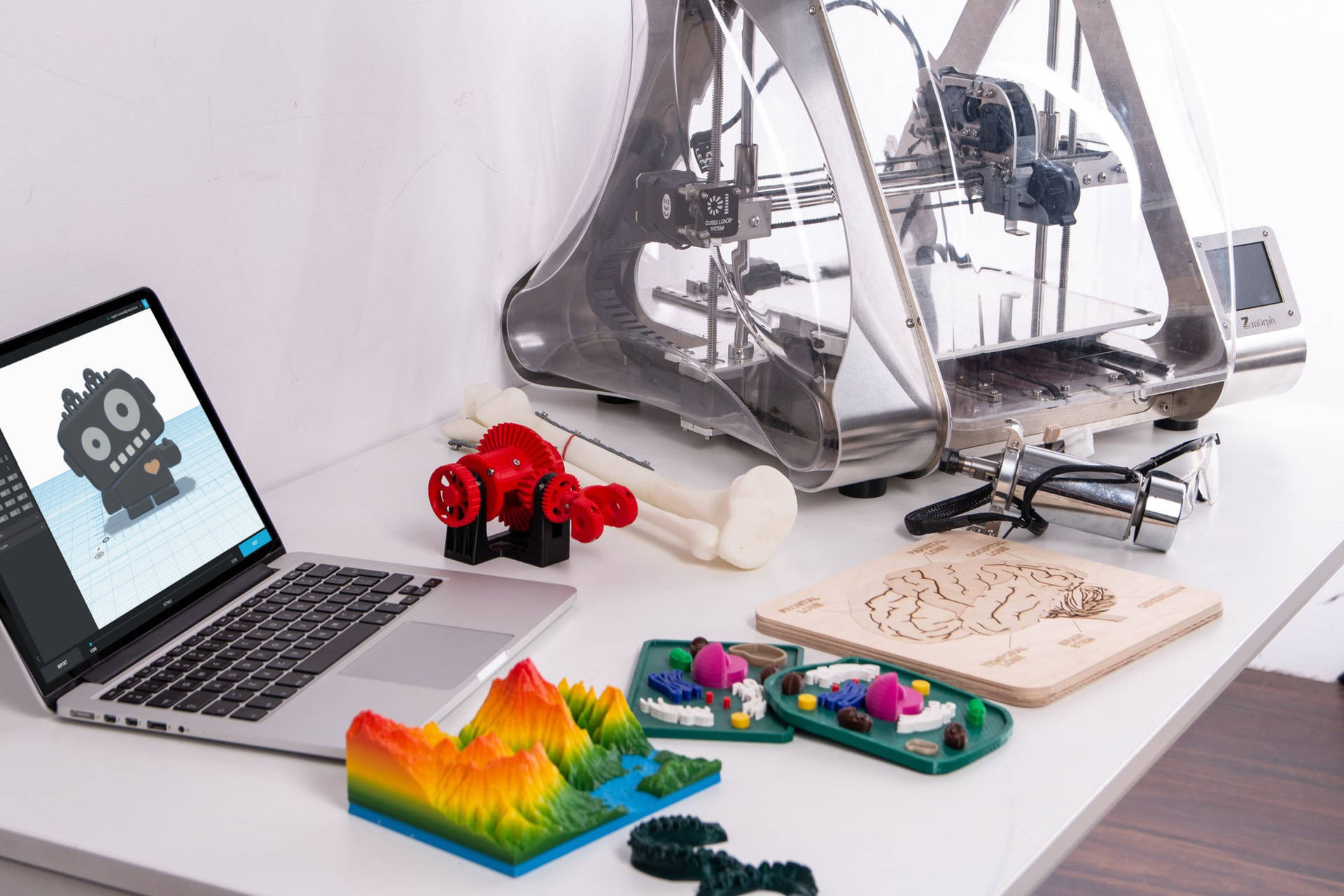 桌子上的3D打印機、筆記本電腦和色彩繽紛的3D打印模型，包括彩虹山。