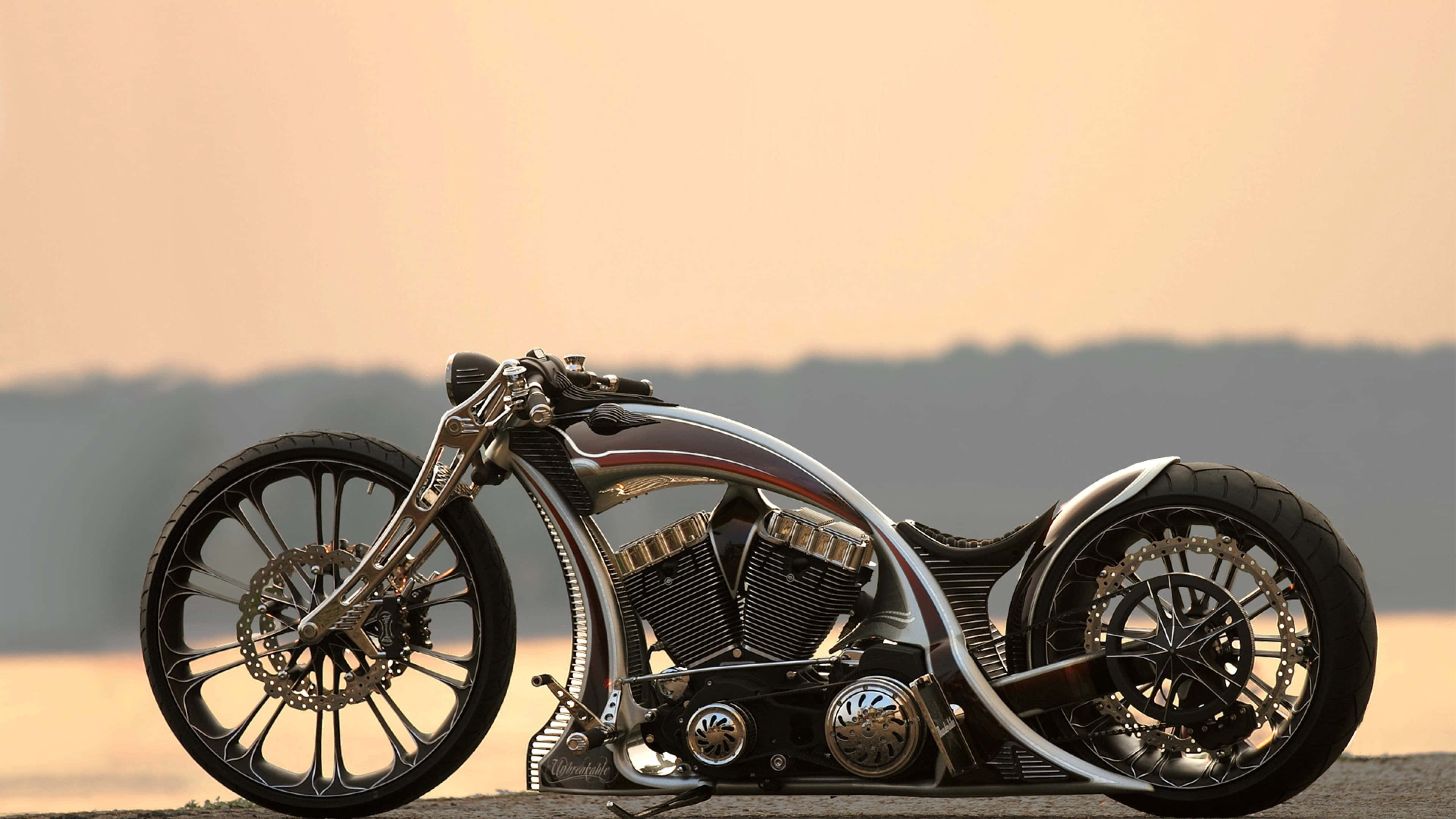 4K自行車——充滿腎上腺素的冒險即將展開 壁紙 — 一架時尚的定制chopper電單車，帶有鍍鉻裝飾和鋼絲輪圈，在日落時停泊在鋪砌路面上。