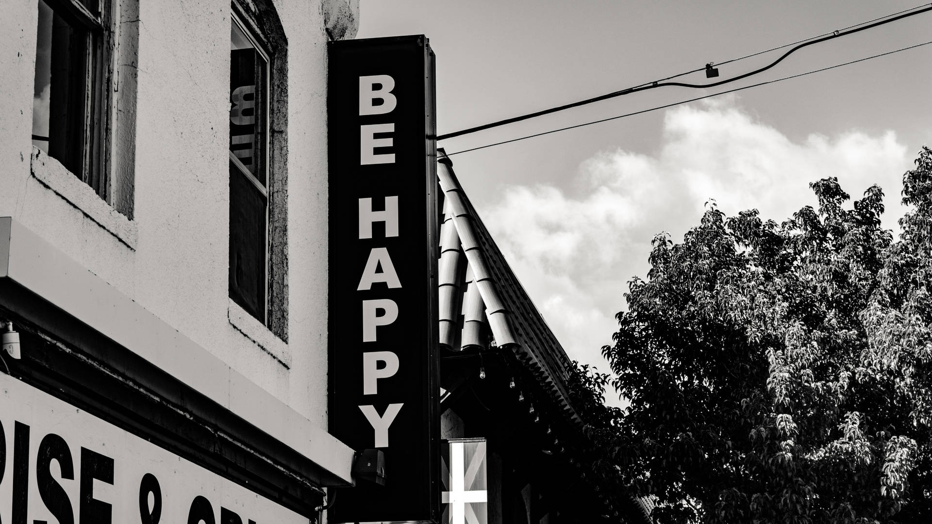 城市建築上寫有「BE HAPPY」的黑白標誌，背景有樹木和雲朵。
