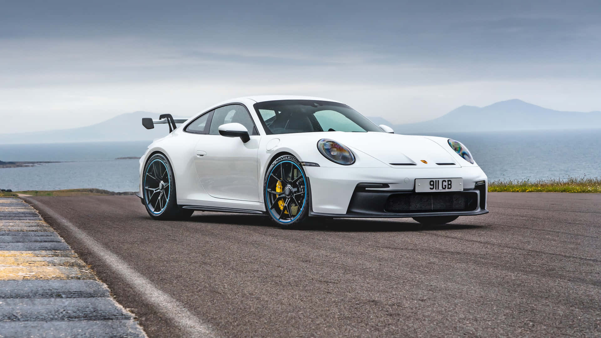 白色保時捷911 GT3 RS行駛於海岸公路，背景為大海和山脈。