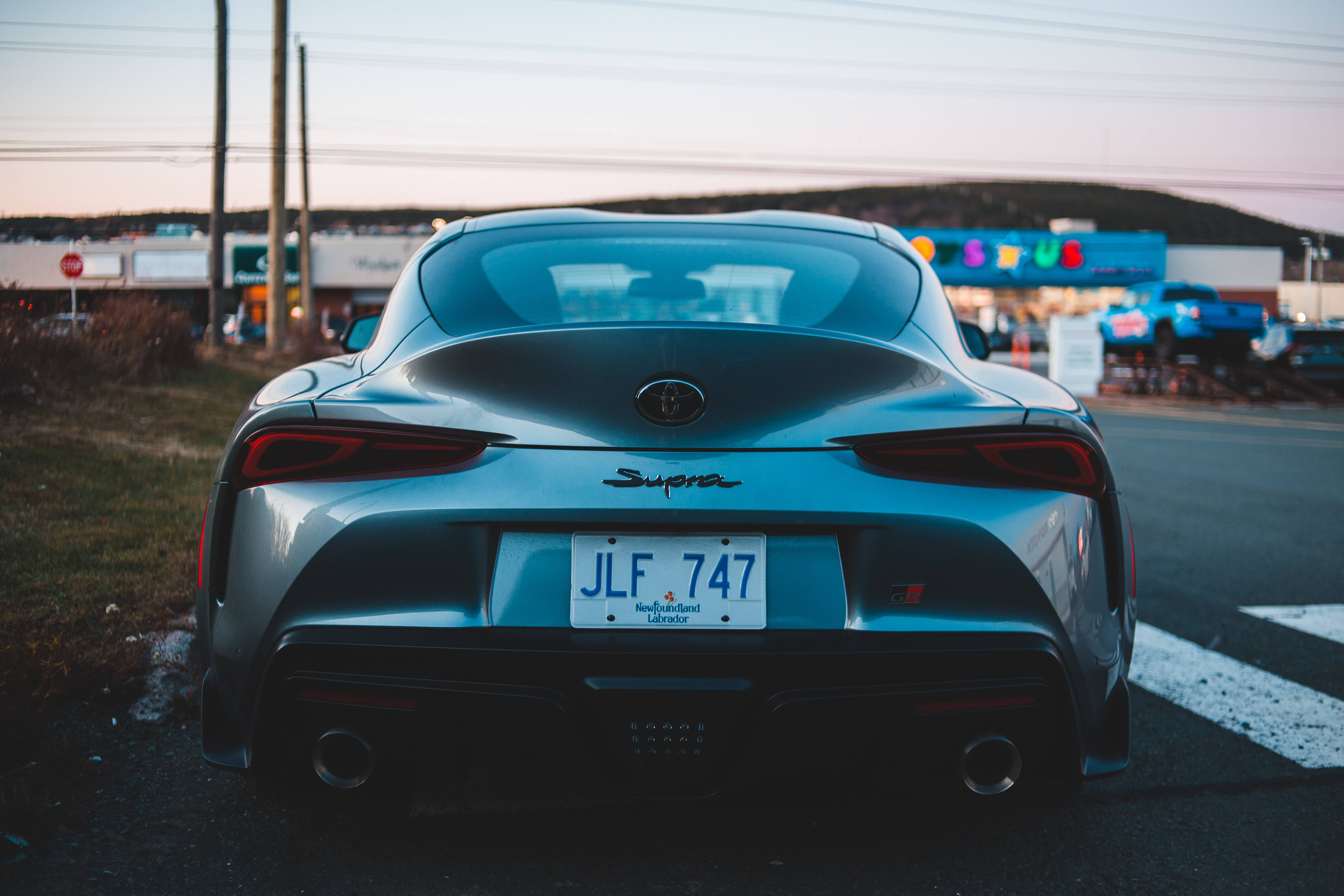 4K閃亮深灰色Toyota Supra 壁紙 — 一輛時尚的銀色豐田Supra在黃昏時停泊，尾燈閃爍，背景是色彩繽紛的霓虹燈牌。