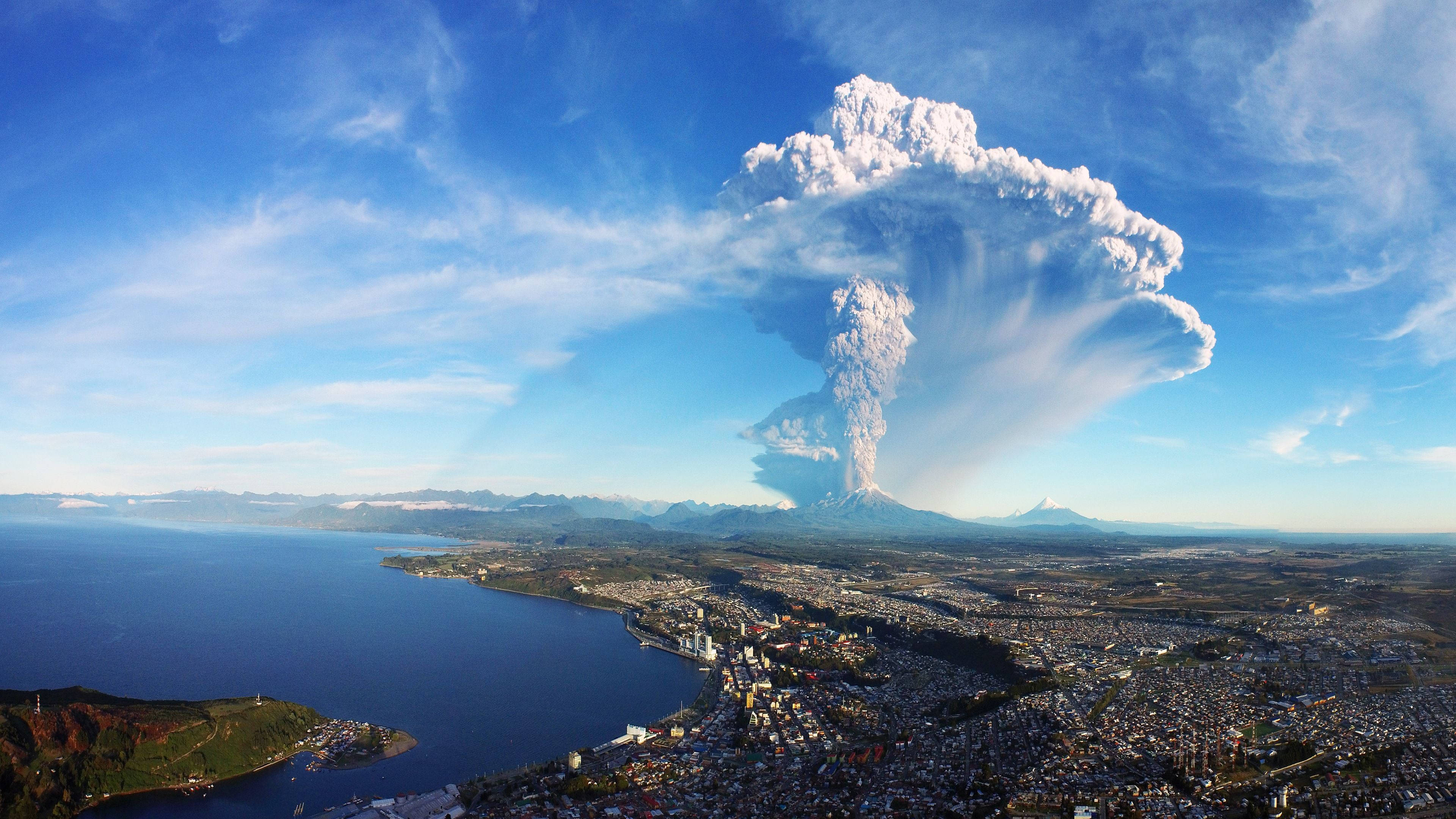 4K電腦火山爆發 壁紙 — 大規模火山爆發，在沿海城市和海洋上空的清澈藍天中噴出高聳的火山灰柱。