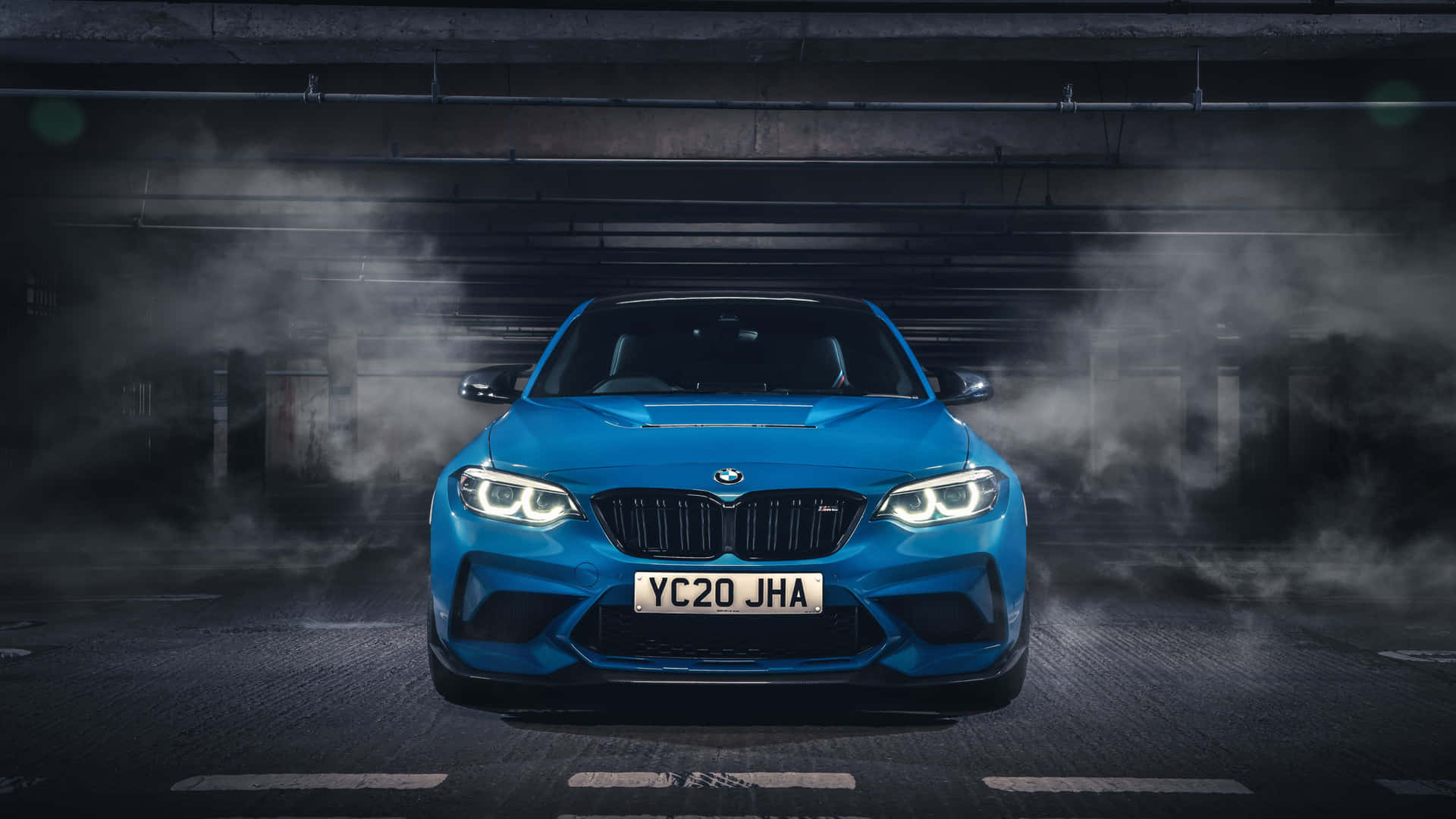 藍色BMW M2跑車在煙霧瀰漫的地下車庫中亮著車頭燈。